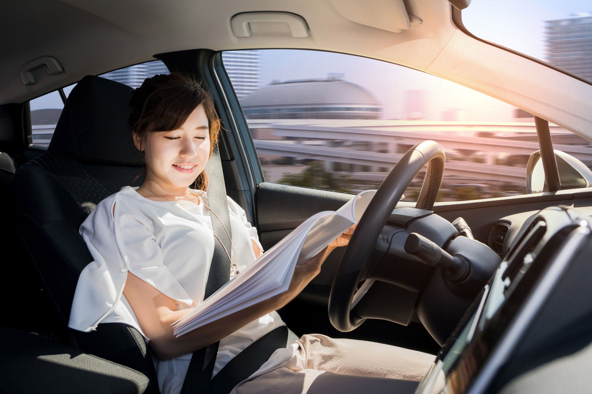 Young woman reading a magazine in autonomous car. Self driving vehicle. Autopilot. Automotive technology.