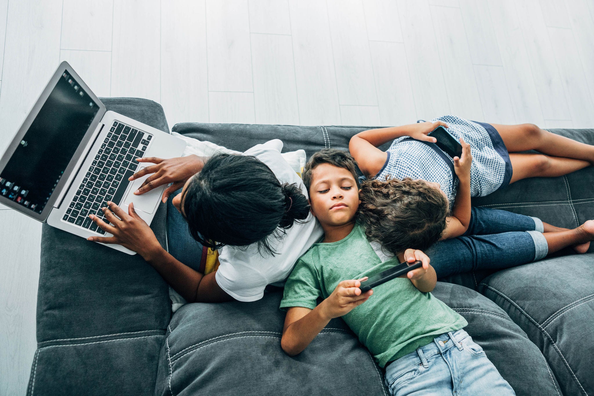 African-american mother using laptop while her two children using smartphones.