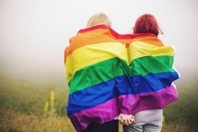 Two women wrapped in a rainbow flag, holding hands