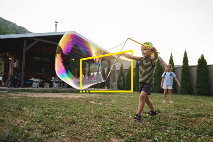 A photograph of a boy making a big soap bubble in the lawn
