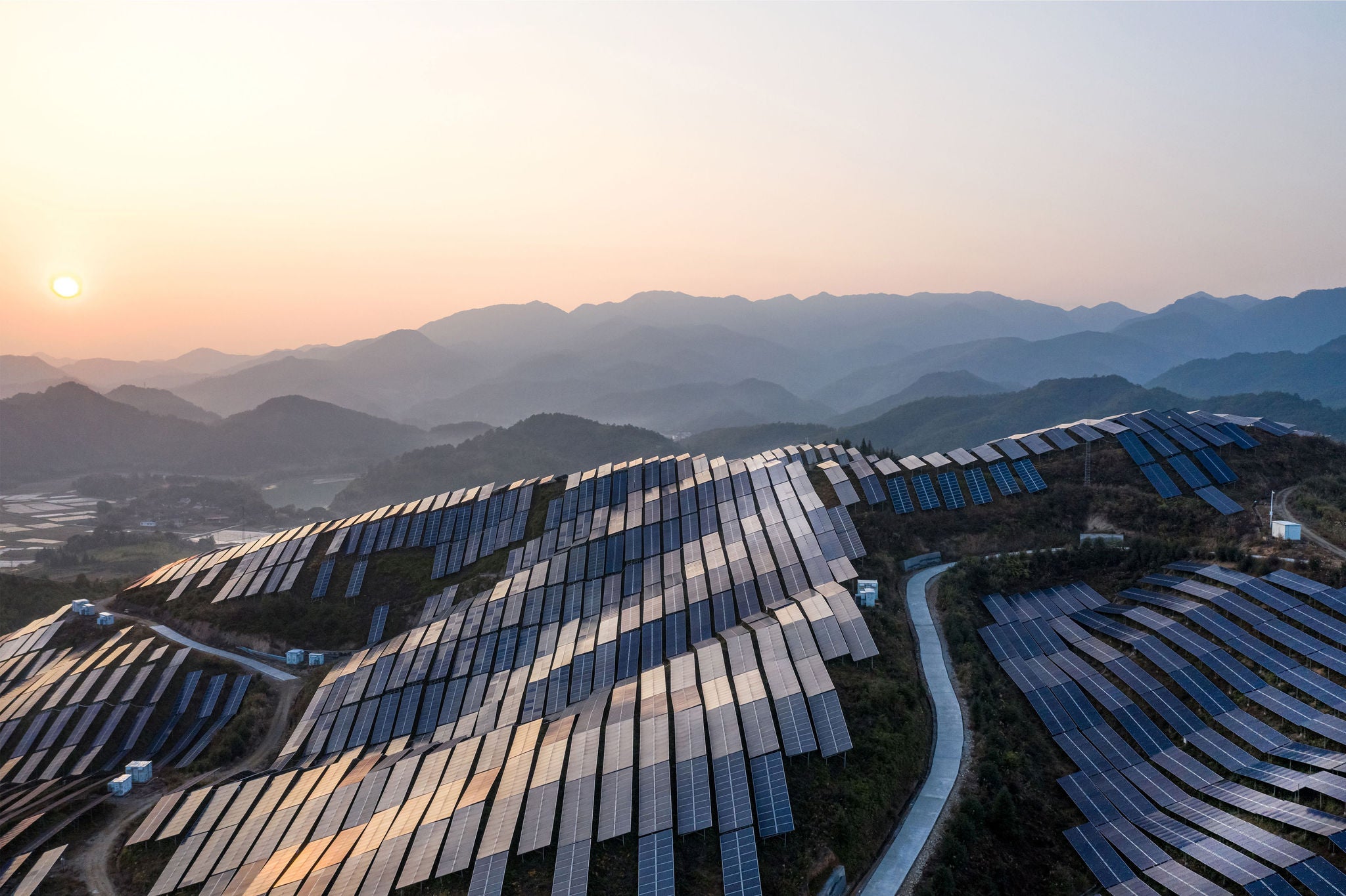 A large solar farm sprawled across hilly terrain, with rows of solar panels capturing sunlight.