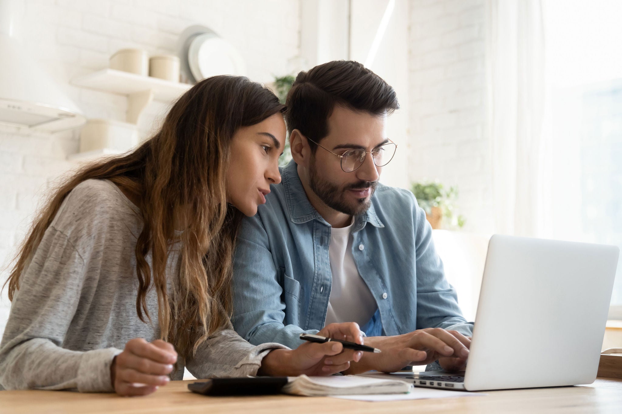 Focused young couple calculating bills, discussing planning budget together, serious wife and husband looking at laptop screen, using online banking services and calculator, checking finances