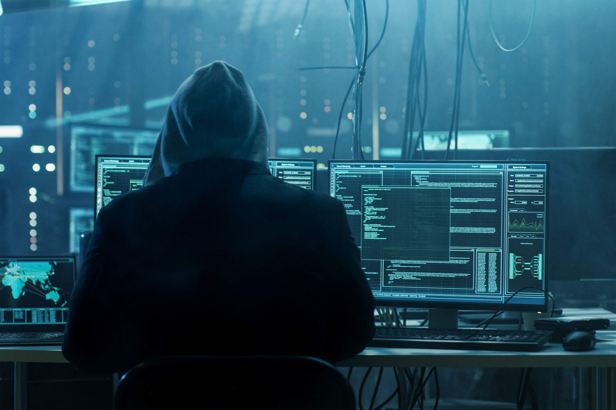 Dangerous Hooded Hacker Breaks into Government Data Servers and Infects Their System with a Virus. His Hideout Place has Dark Atmosphere, Multiple Displays, Cables Everywhere.