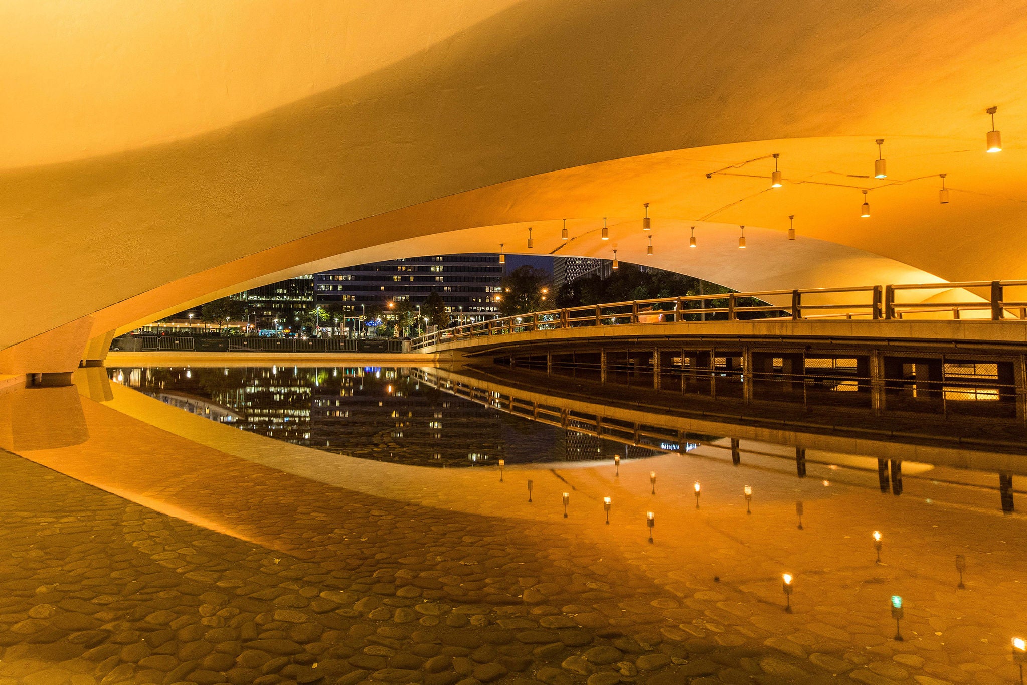 Walkway over water under a city bridge.