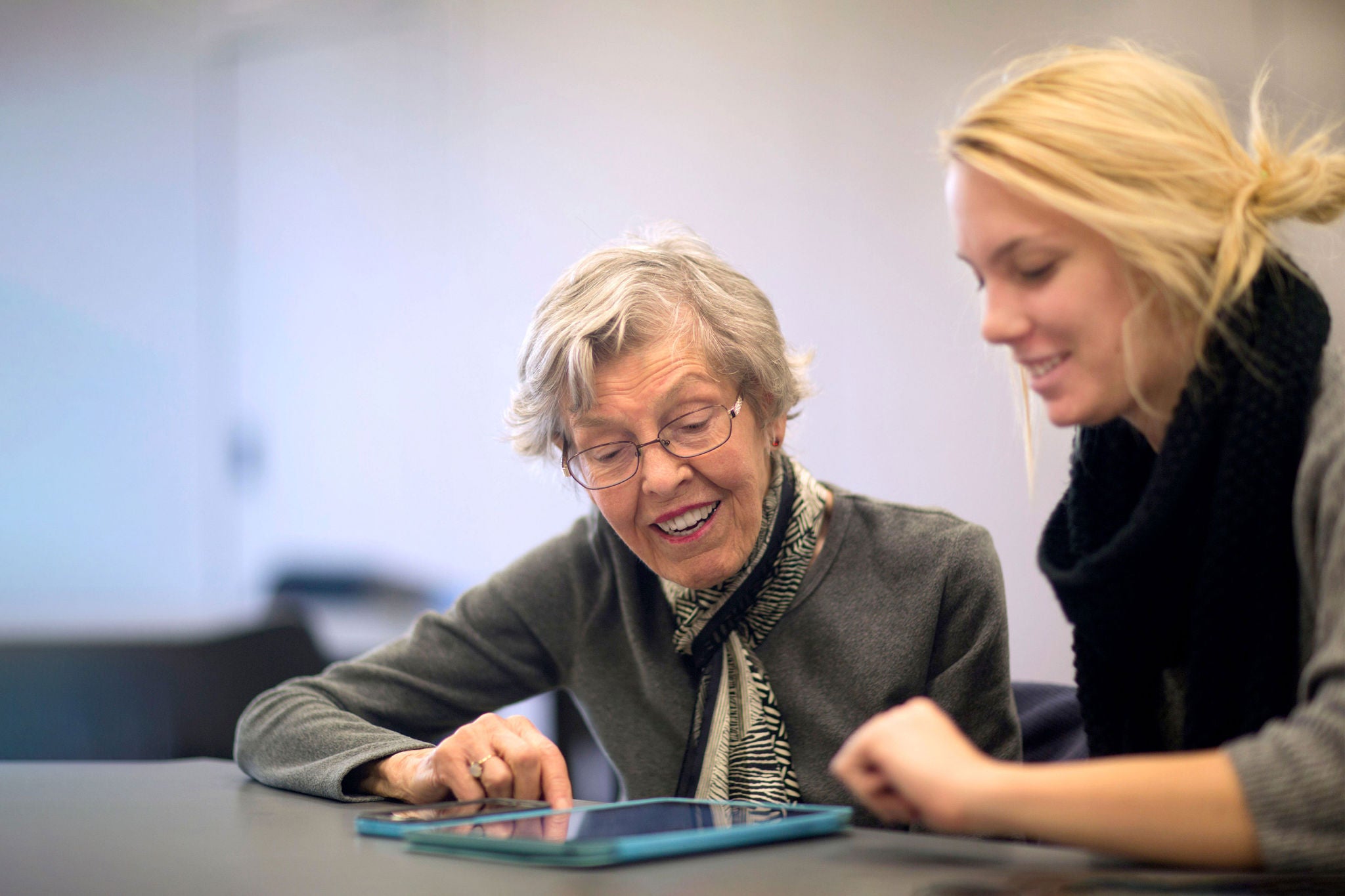 Young woman helps senior adult with tech devices.