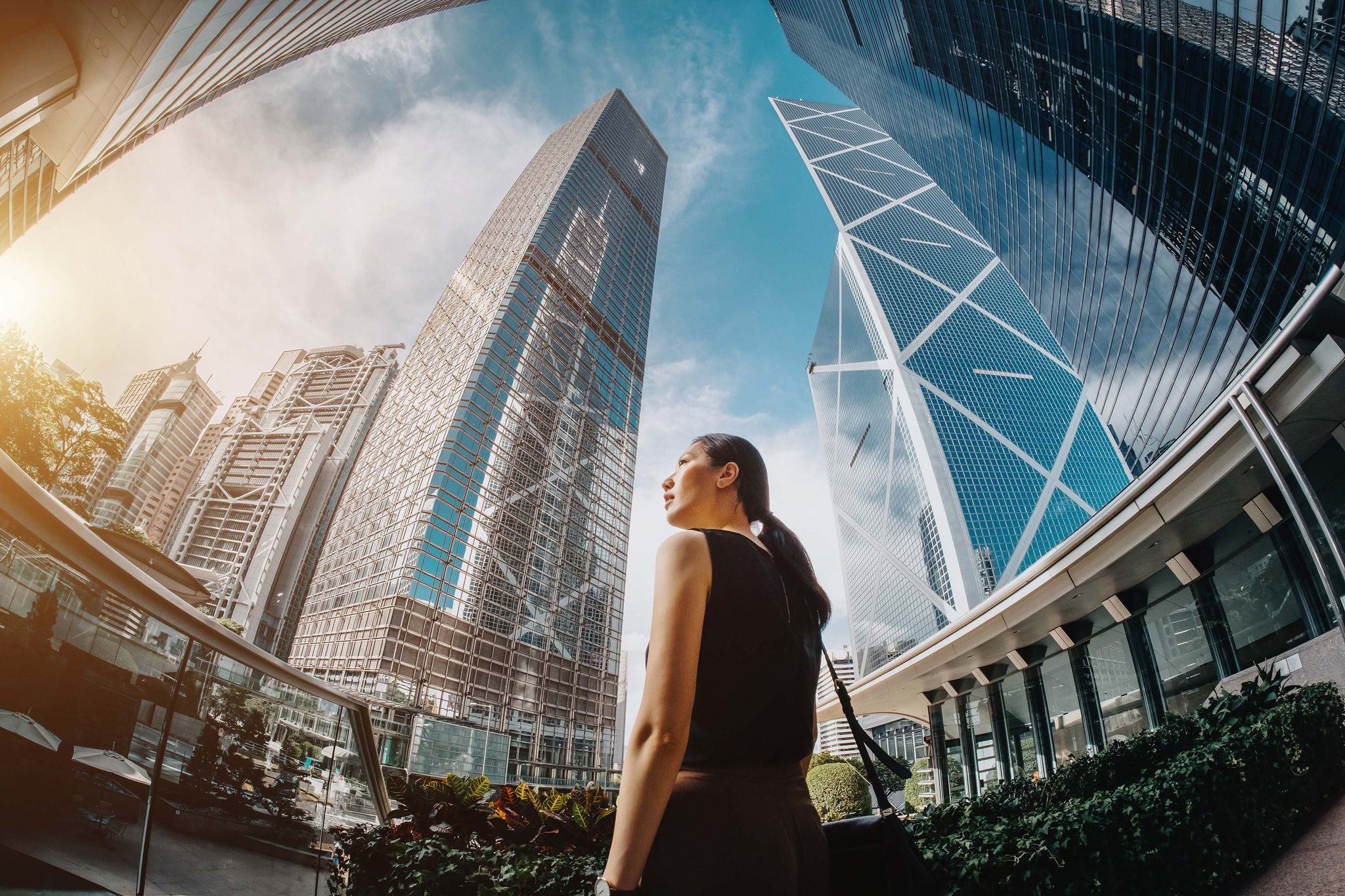 Professional Asian businesswoman standing against highrise financial towers in Central Business District and looking up into sky with confidence