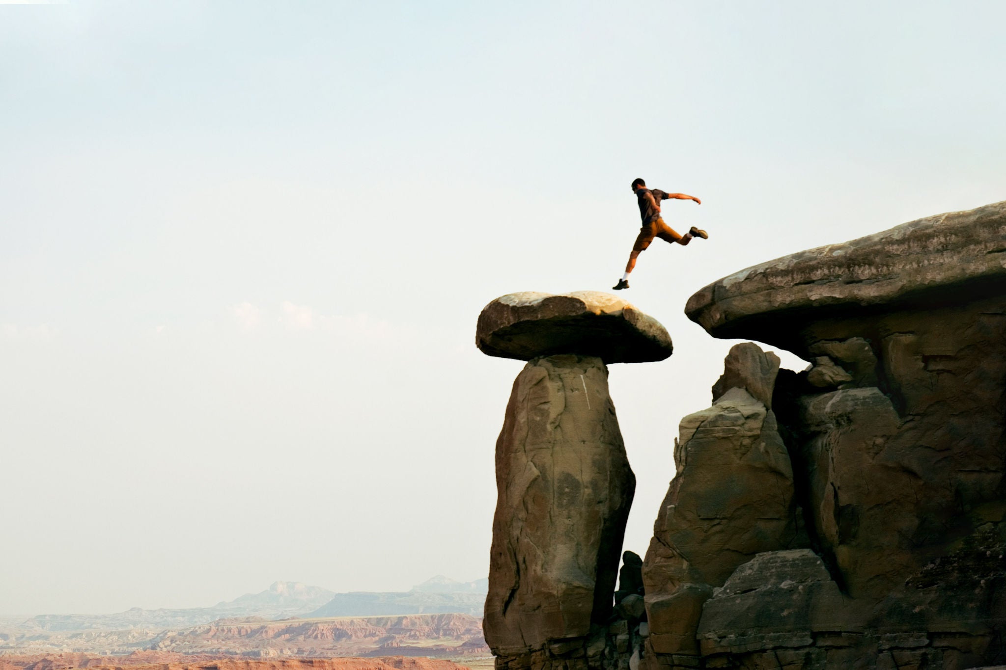 A young man jumps across a set of  rocks in moab utah background