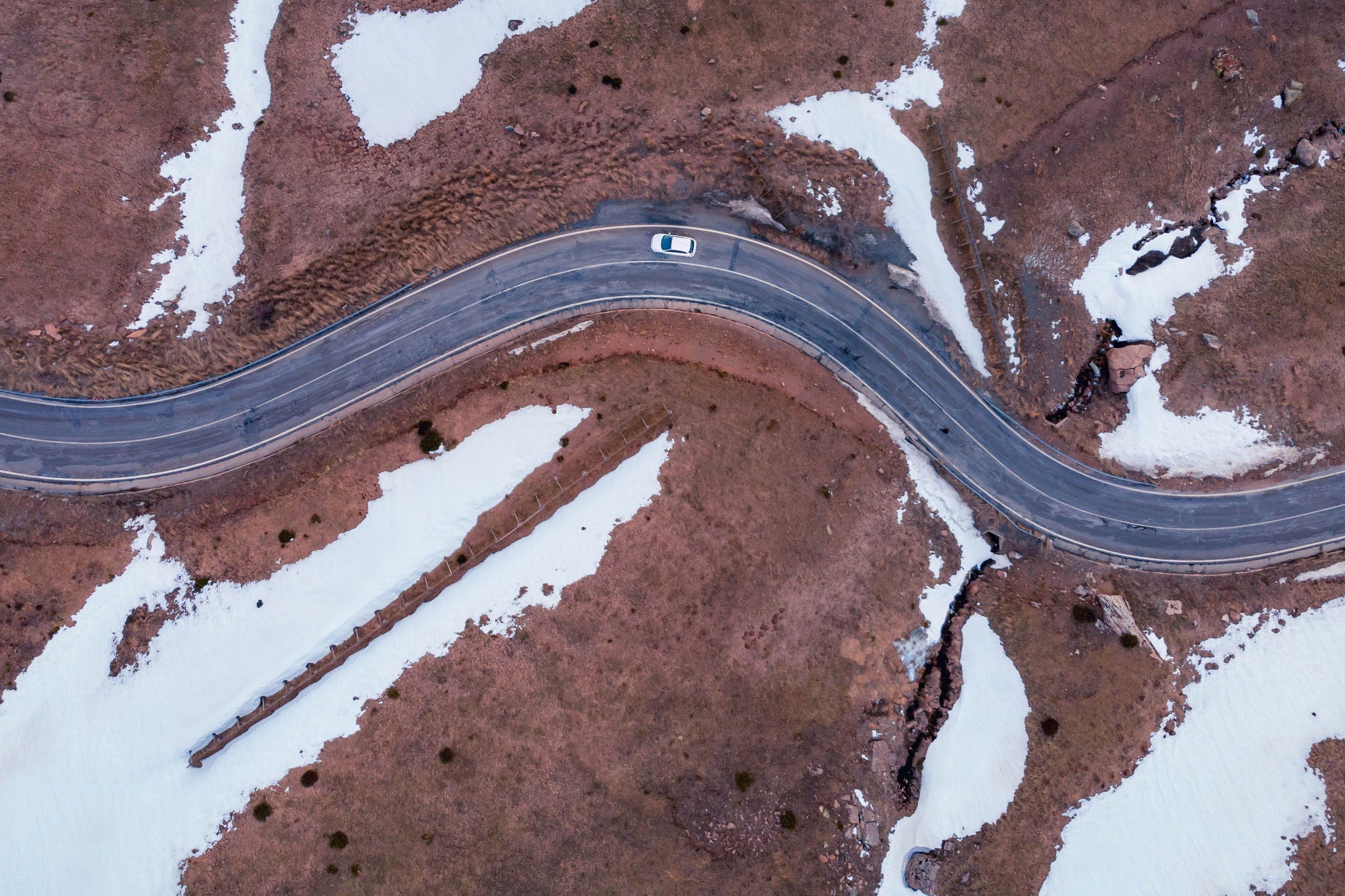 From above aerial view of a curving road surrounded by patches of snow with a vehicle traveling along it in Cerler, Huesca, Spain