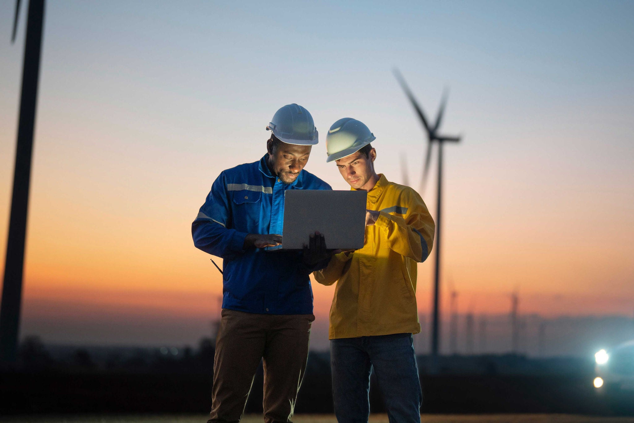 Junges Team von Wartungsingenieuren bei der Arbeit in einem Windkraftpark bei Sonnenuntergang