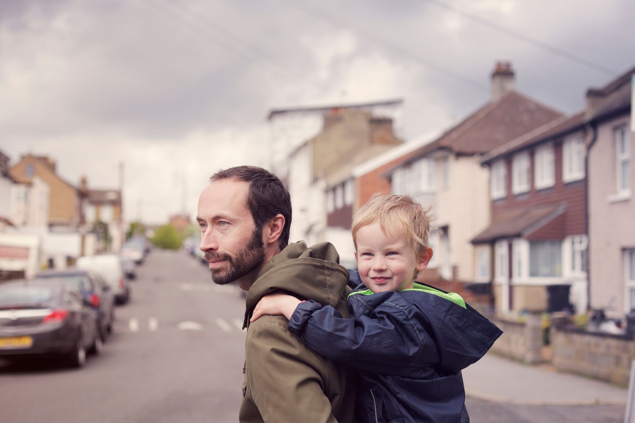 A father carrying his young son on his back while crossing a road on the school run.