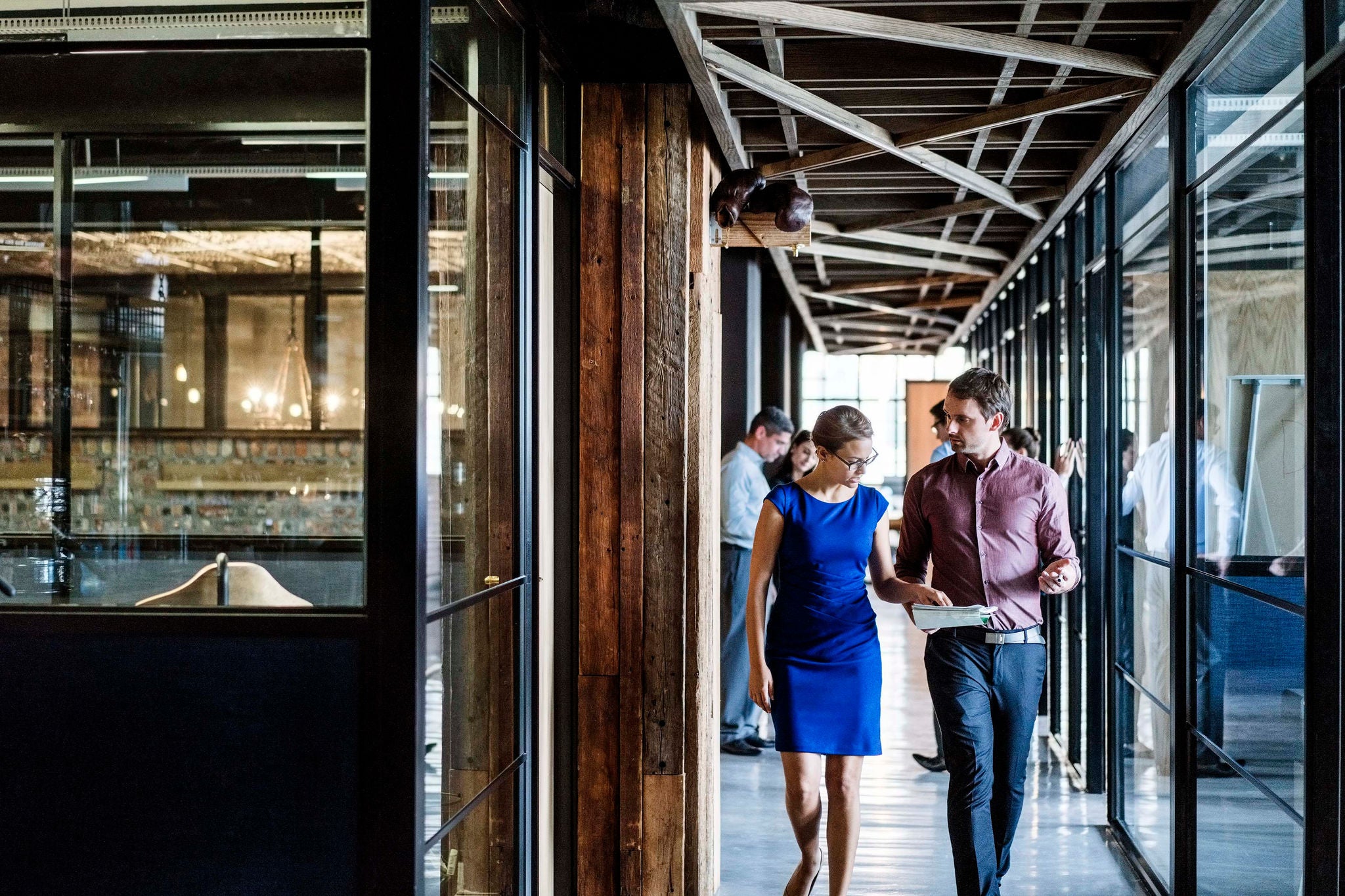 Business people walking in corridor. Male and female professionals reading documents. They are in formals at office.