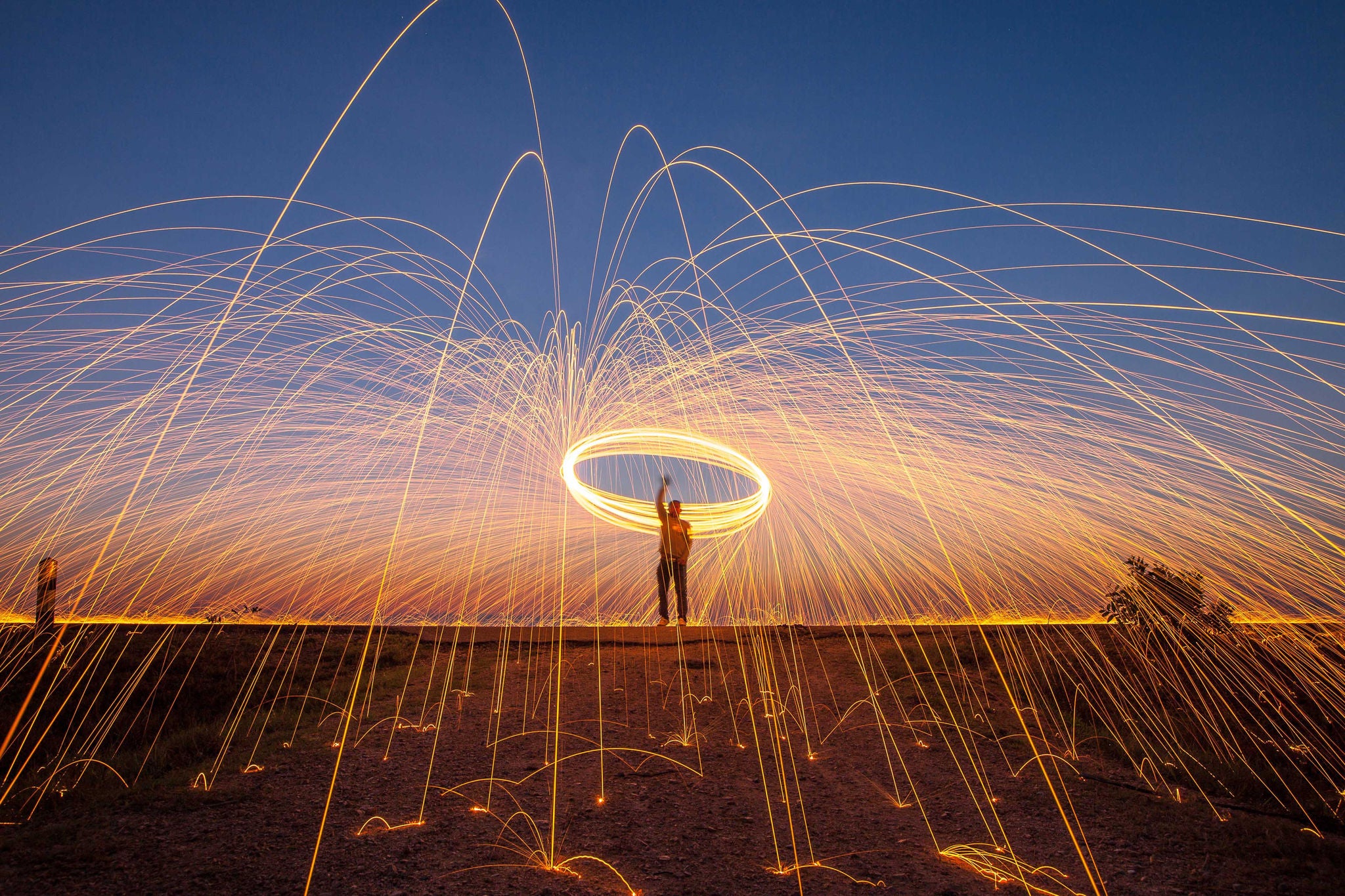 Hombre en un campo abierto realizando círculos con chispas luminosas