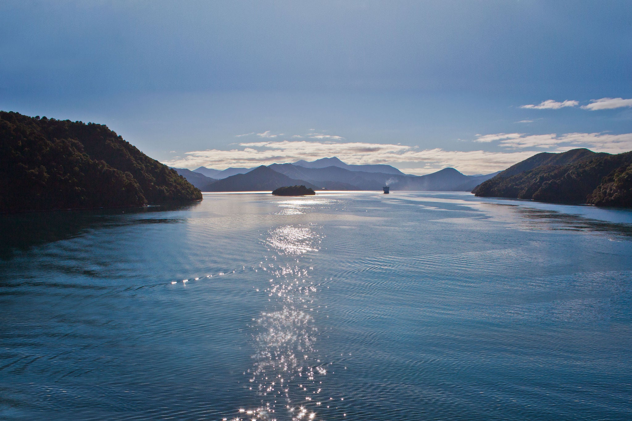 A serene water body surrounded by forested hills and mountains.