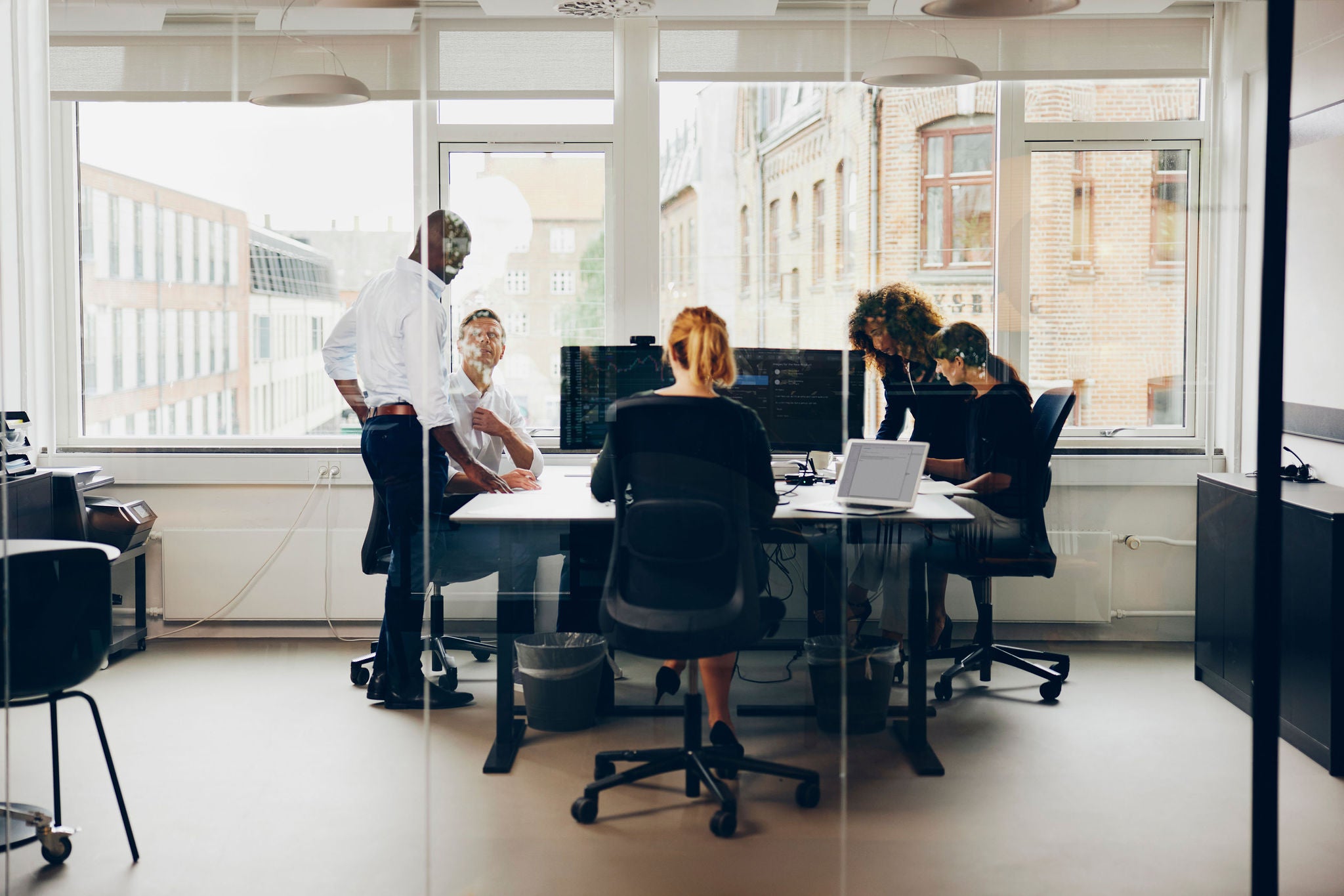 Diverse group of businesspeople working together on computers around some desks inside of an office