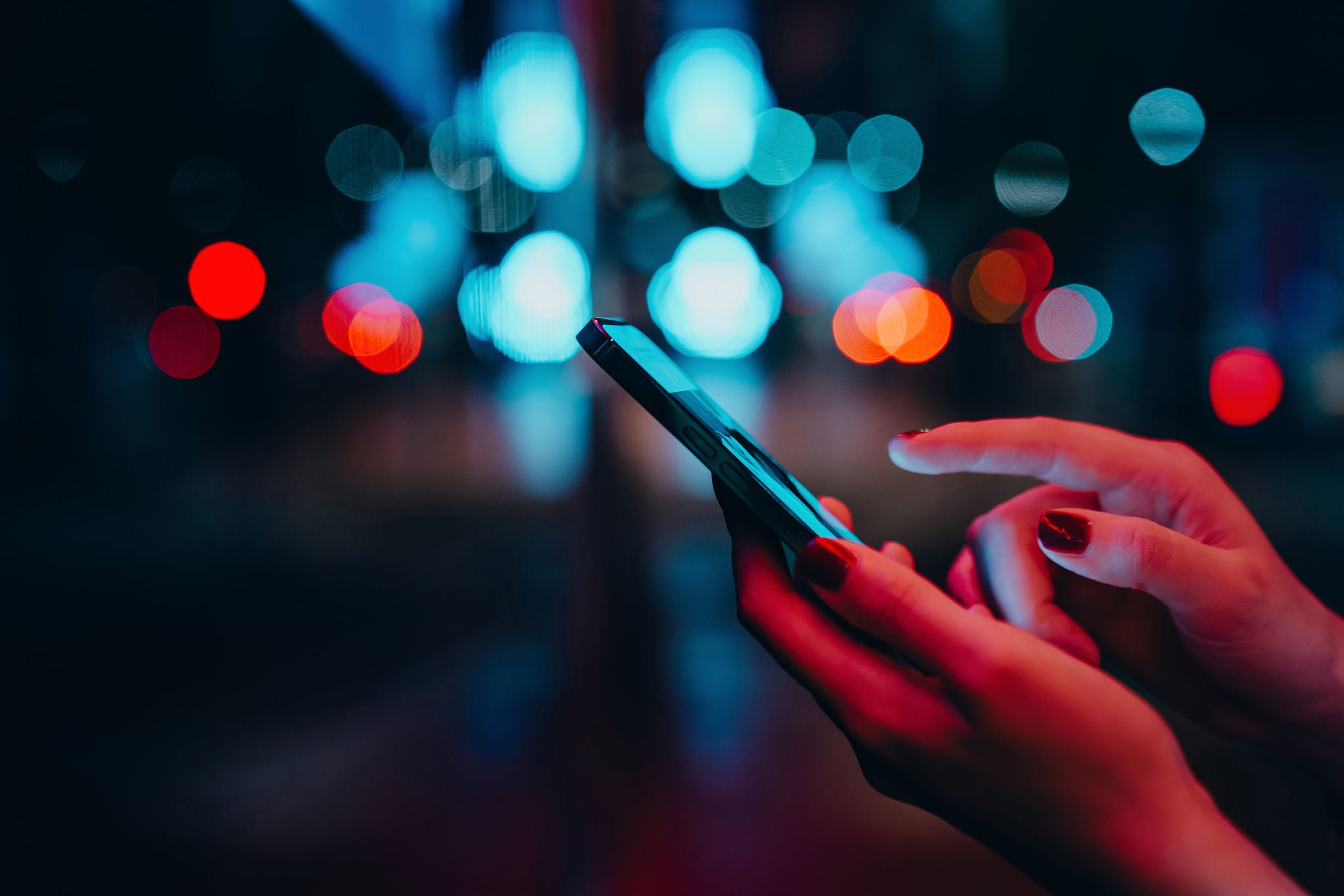 Young woman networking with social media on smartphone in city street at night. 