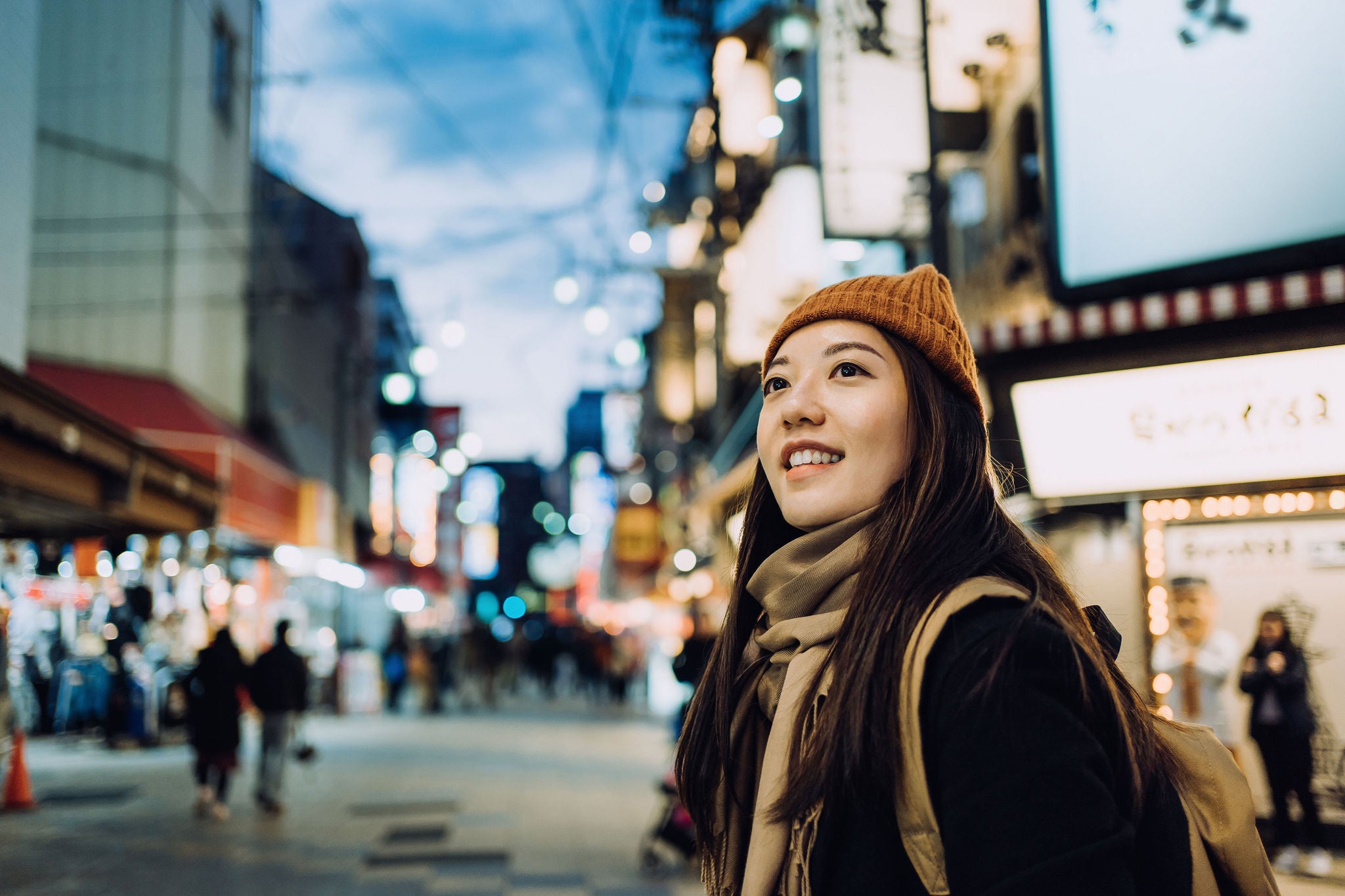 Smiling young Asian female traveller exploring and strolling in busy local city street at night in Osaka, Japan