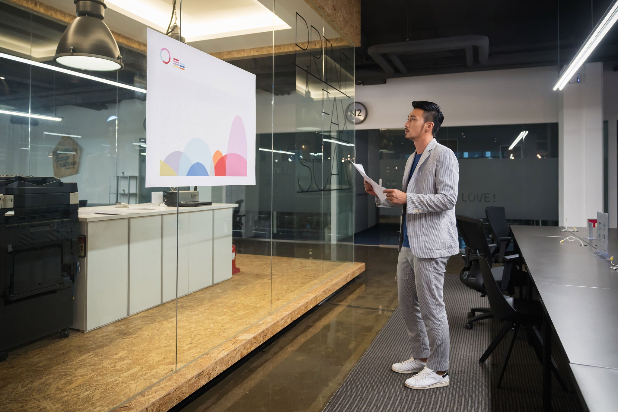 An Asian creative worker analyzing a informative graph on glass wall in high tech office.