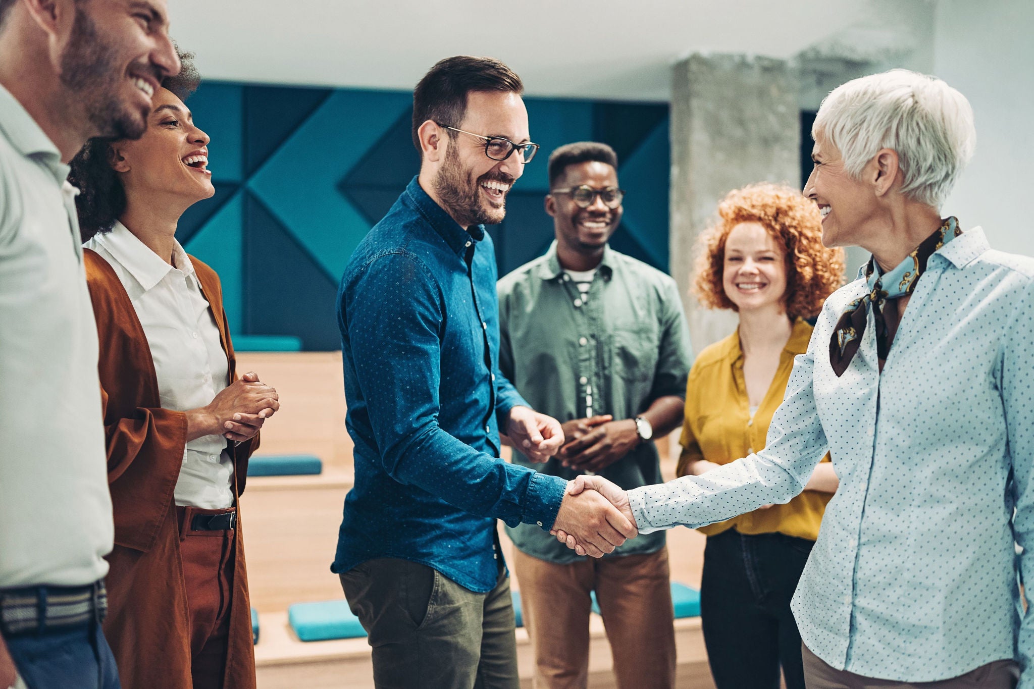 Photograph of a man and woman shaking hands surrounded by other approving adults