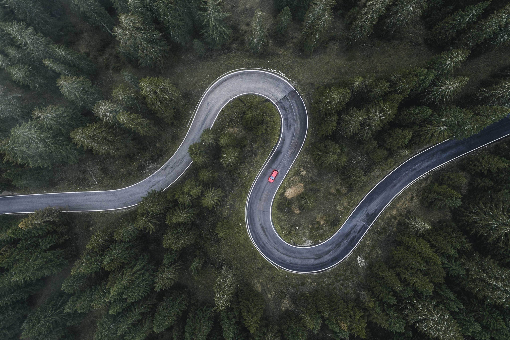 Winding forest road seen and a car shot by drone