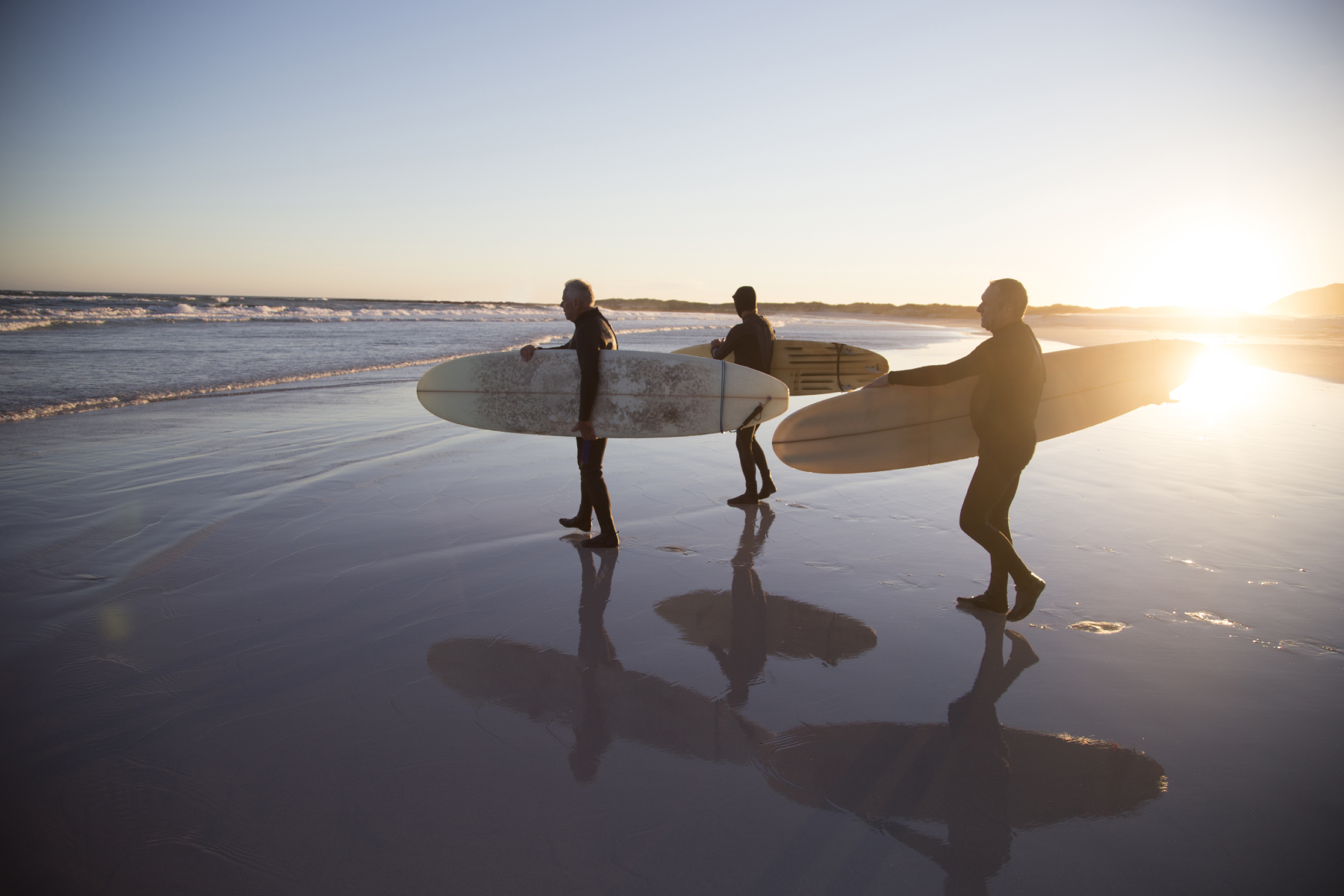 Three senior surfers walking along a sandy beach