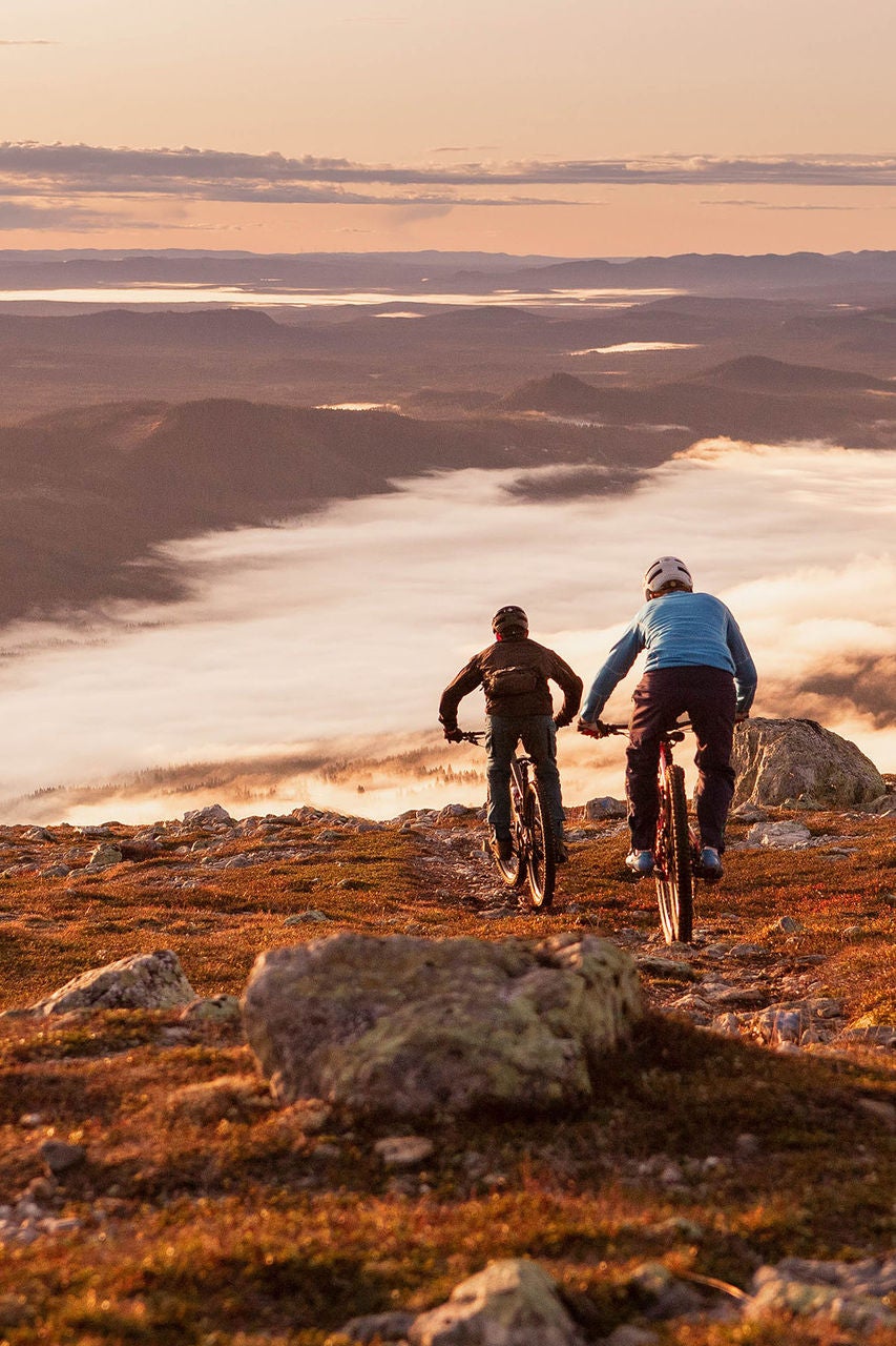 mountain bikers on a hillside looking over a misty valley
