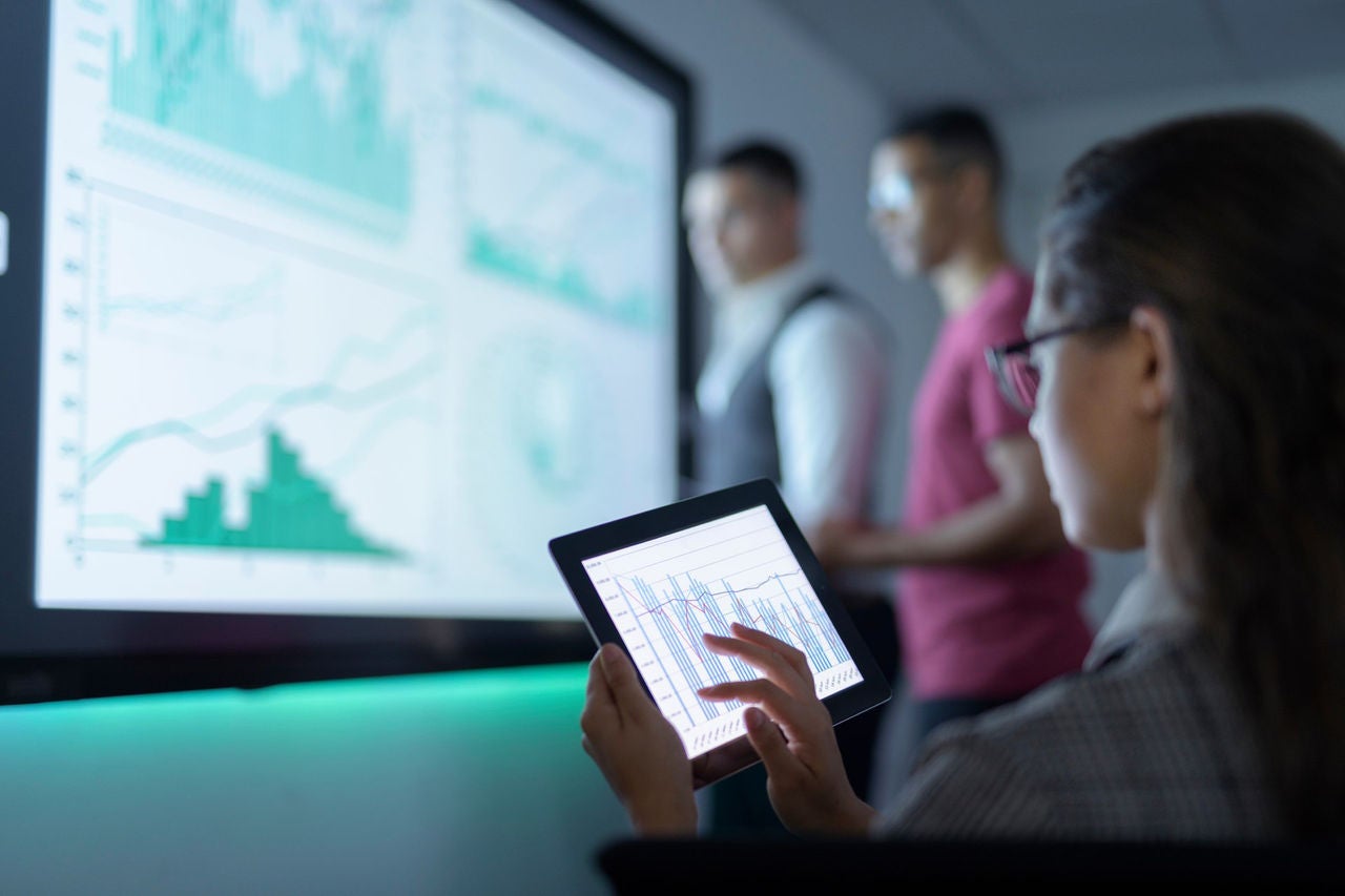 a woman with a tablet reflecting data on a big screen