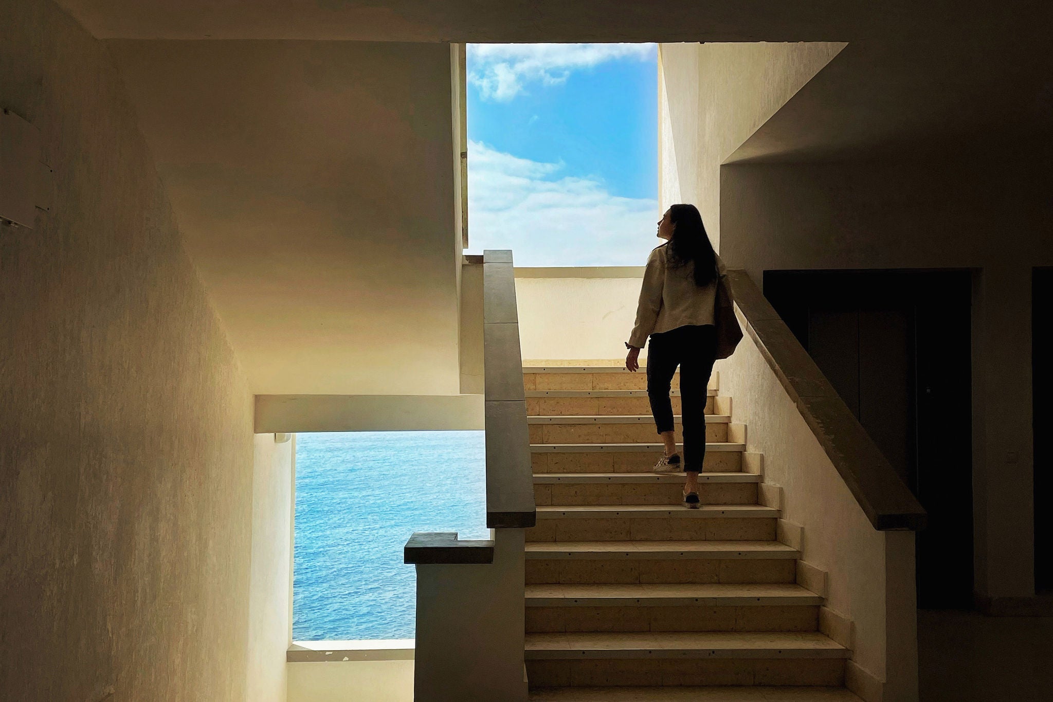 Rear view of woman walking on staircase, from sea to the sky