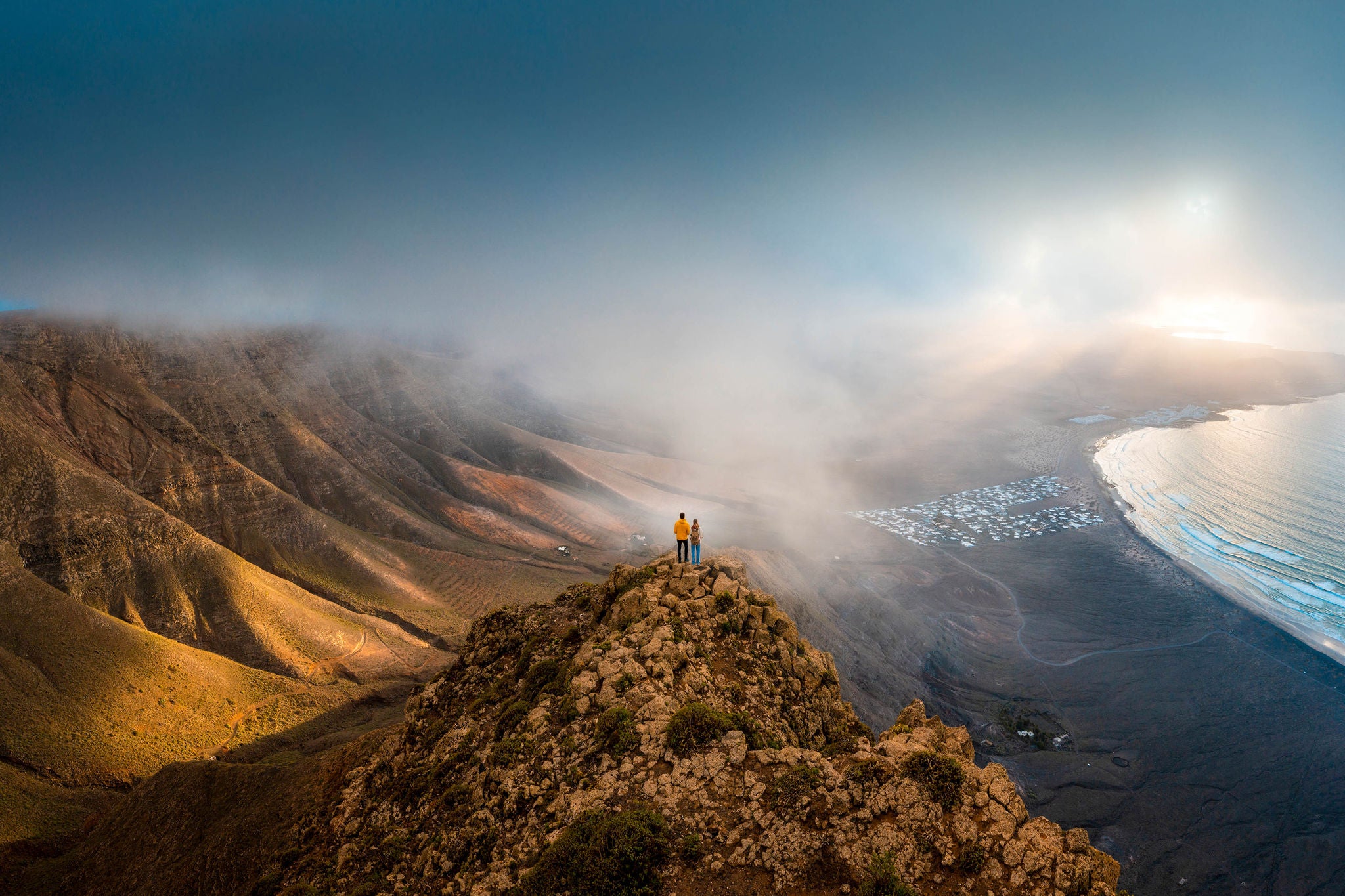 Couple standing on top of a cliff looking at sunset, Lanzarote, Spain