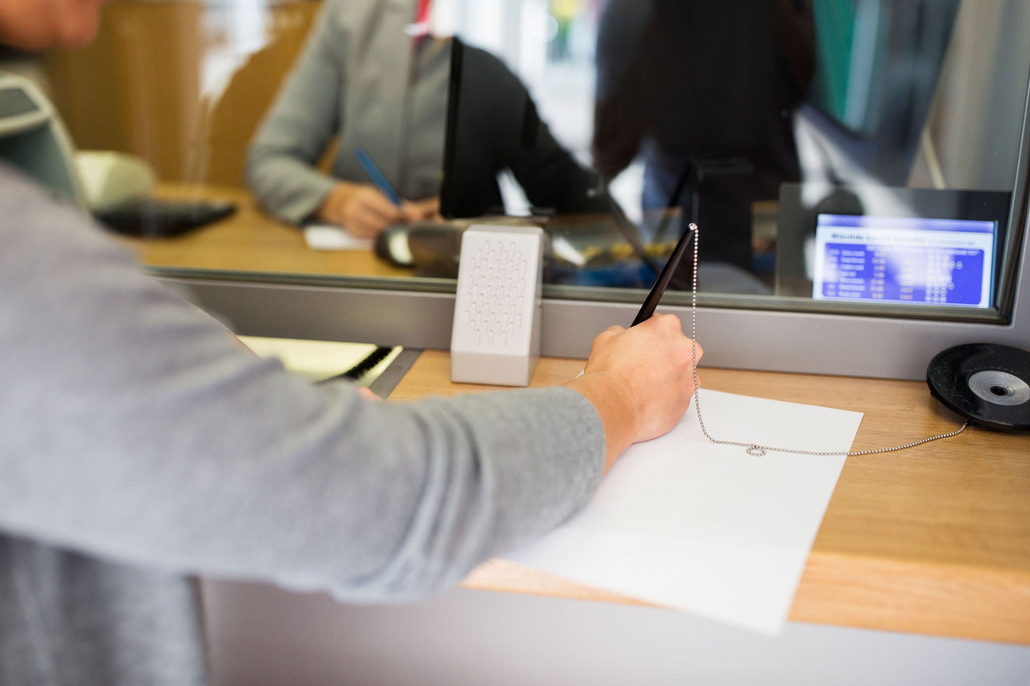 People and finance concept - customer with pen and paper writing application at bank office