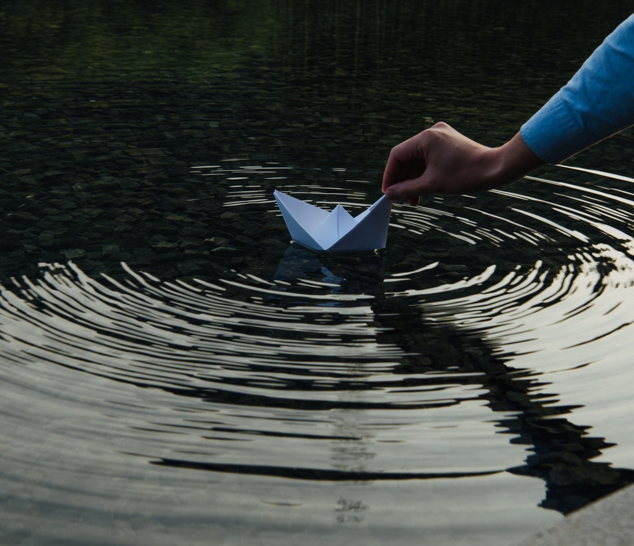 someone placing paperboat in water and its forming ripples