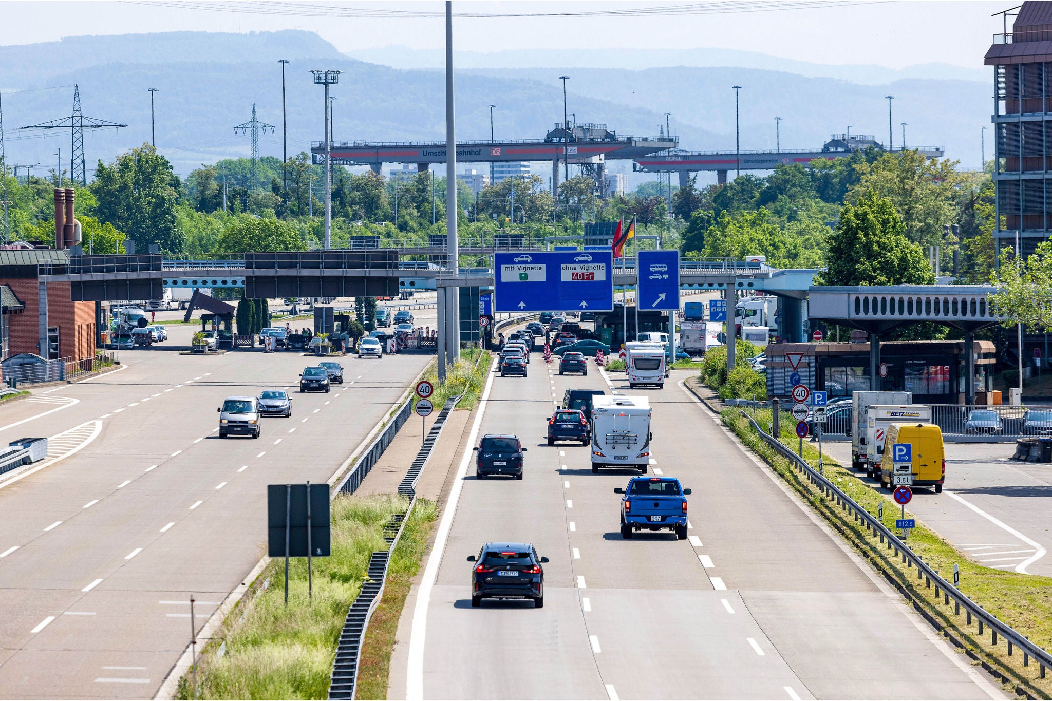 Autos und Wohnmobile fahren auf den deutsch-schweizerischen Grenzuebergang zu. 