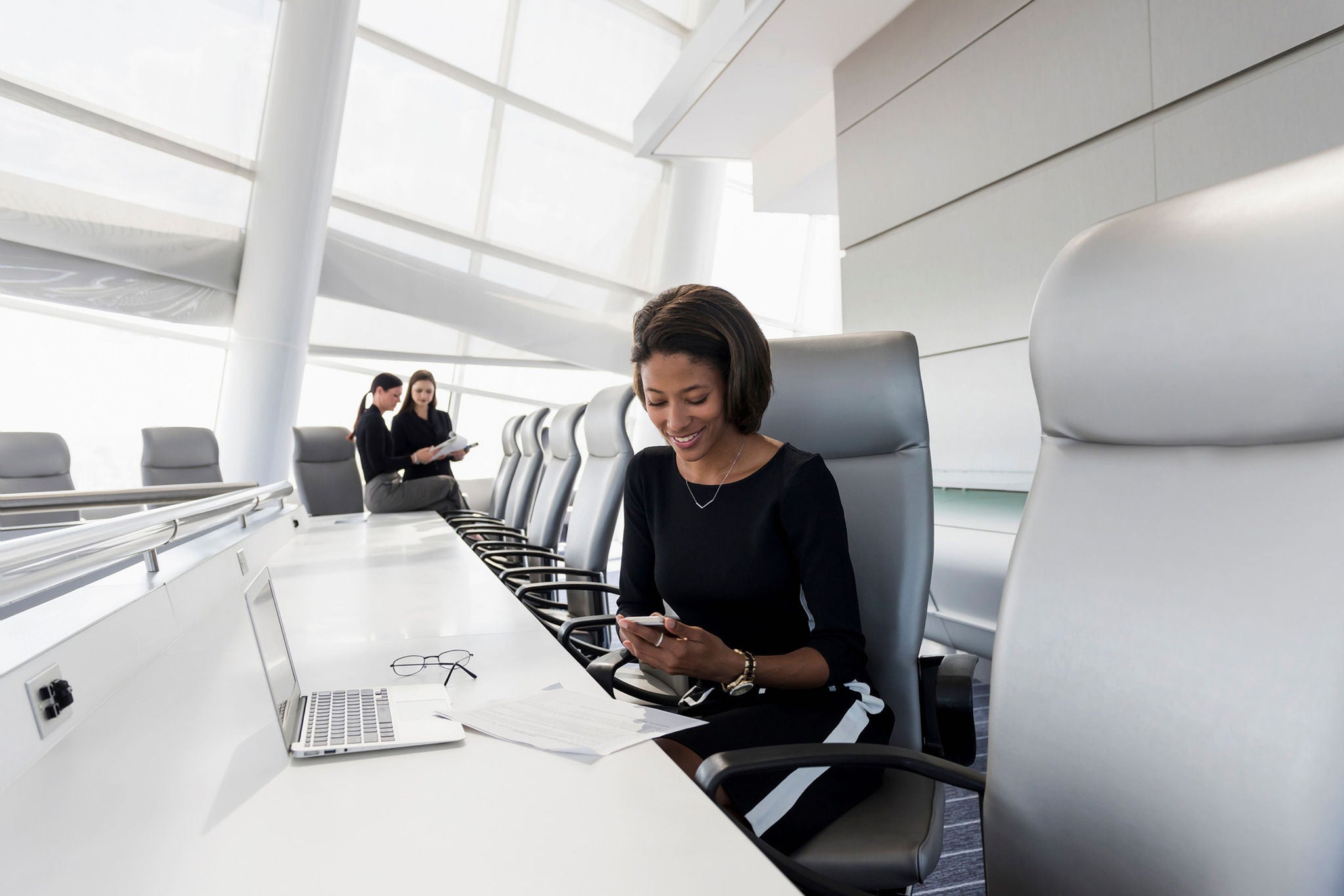 Woman in black dress at meeting table looking at phone and smiling