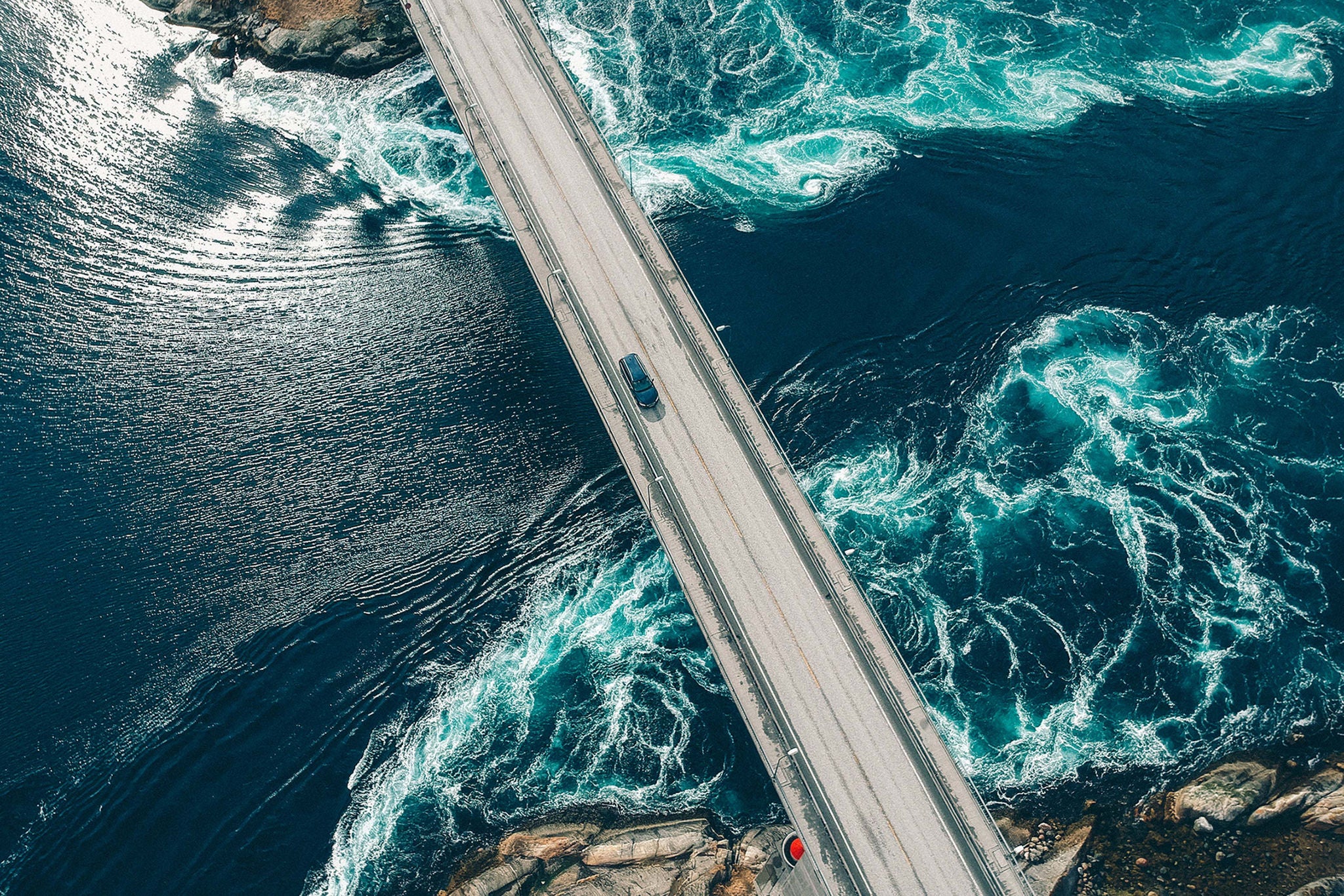 Torrents creating patterns in turquoise water underneath a bridge with a car traveling across it at Salstraumen near Bodo Norway