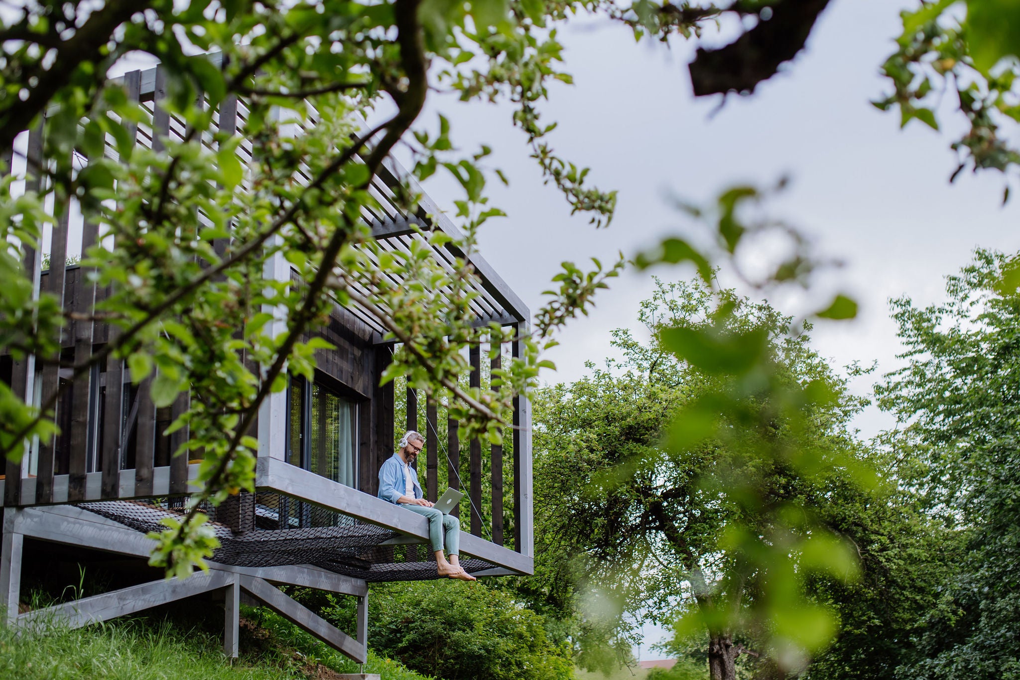 Man with laptop and headphones working outside in tree house. Low angle view.