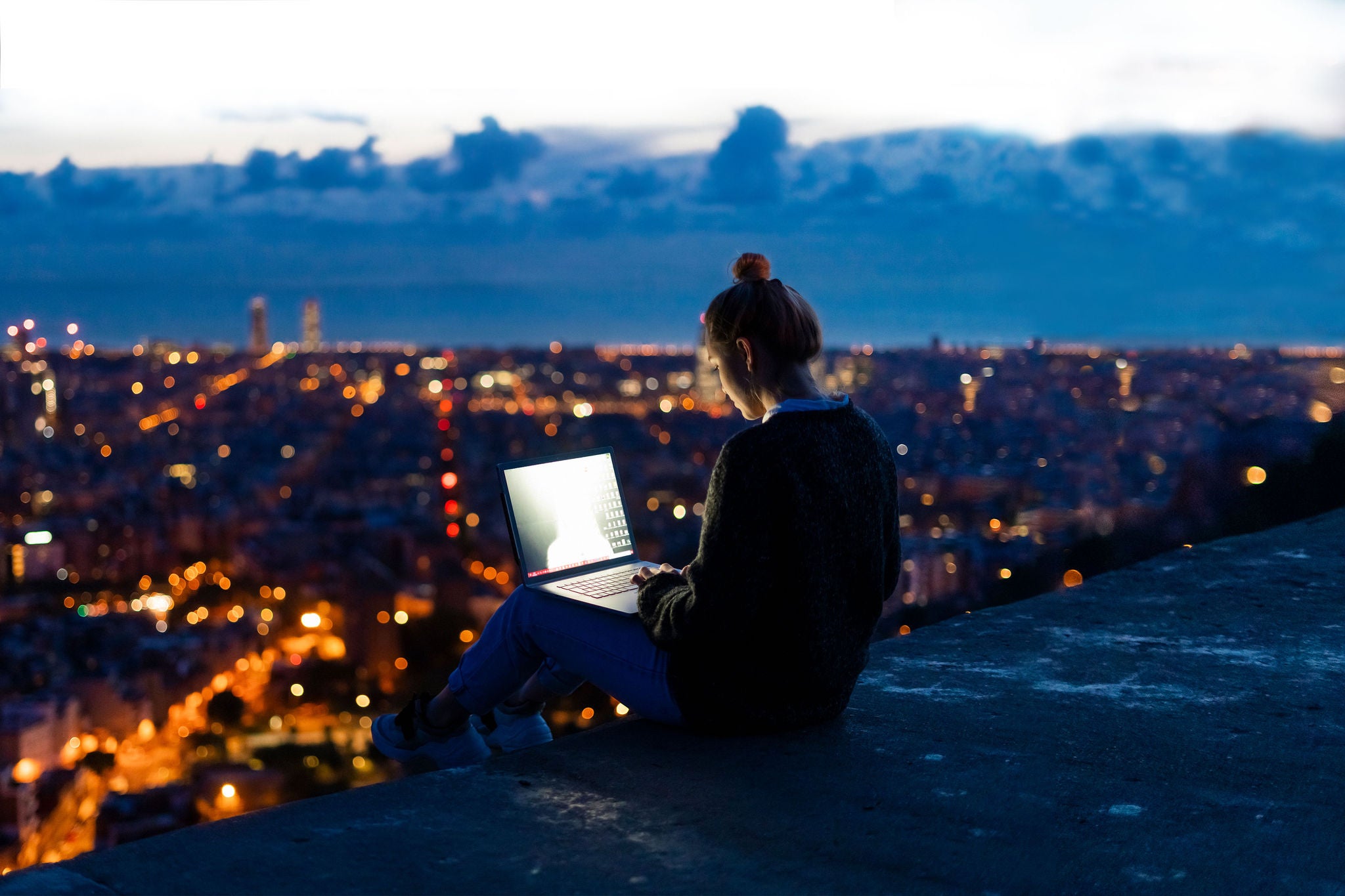 Young woman using laptop at dawn above the city, Barcelona, Spain