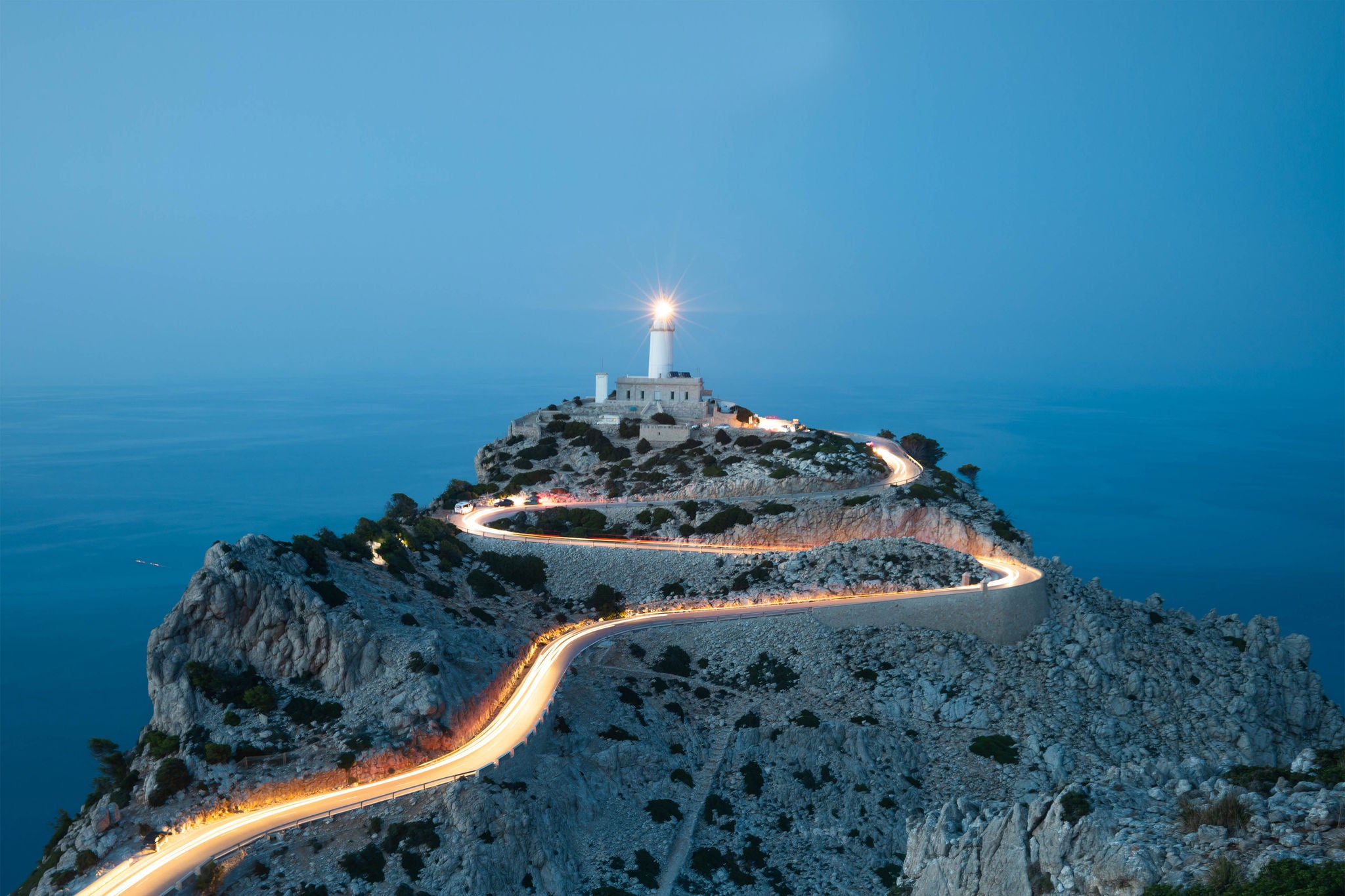 Car light trails in curvy road with lighthouse