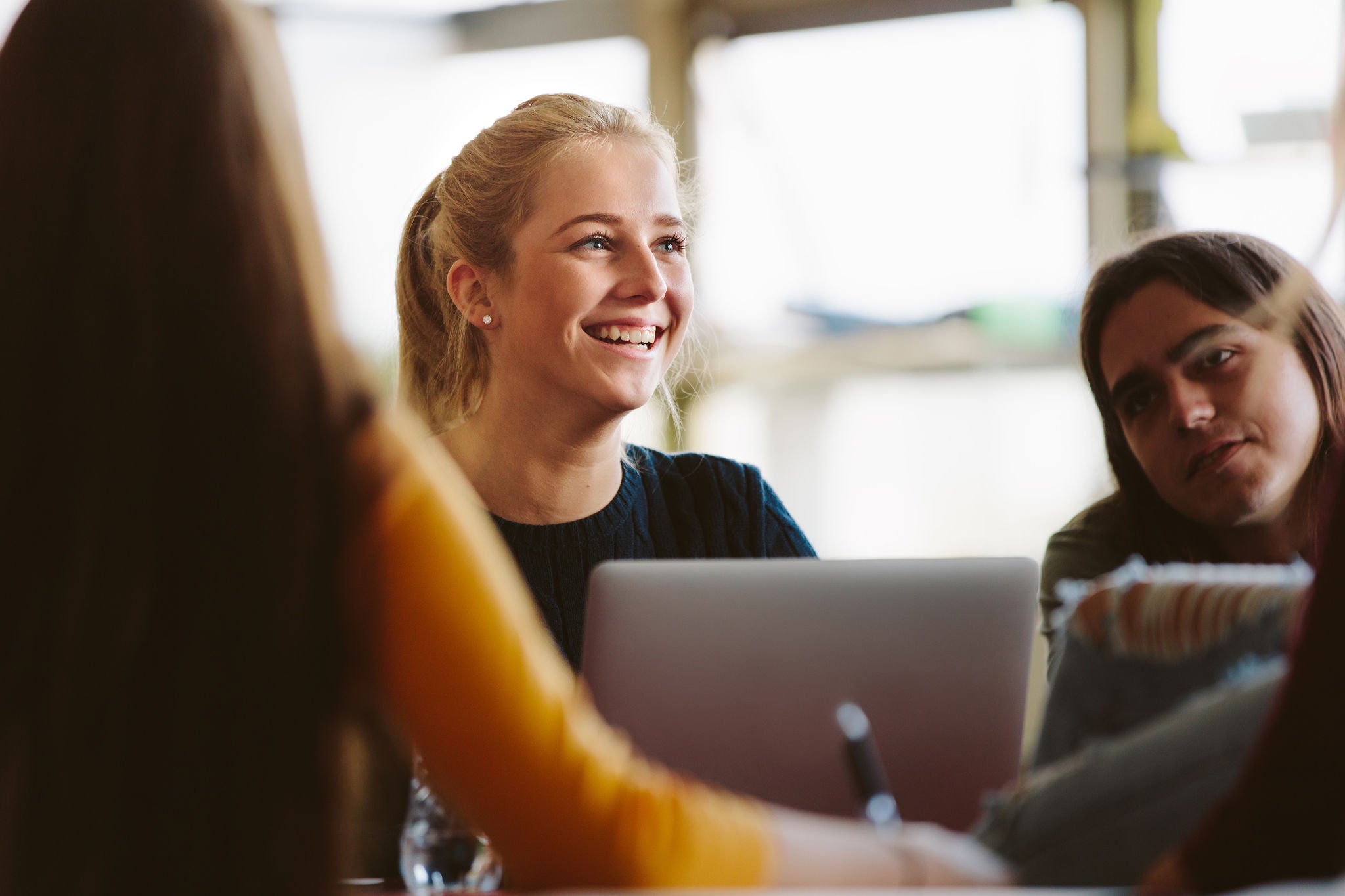 Female student sitting amongst classmates and smiling in lecture room. University students in classroom after lecture.