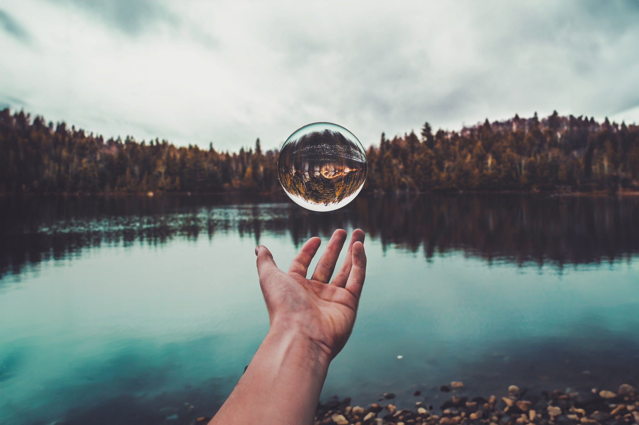 Close-up of hand playing with crystal ball against lake