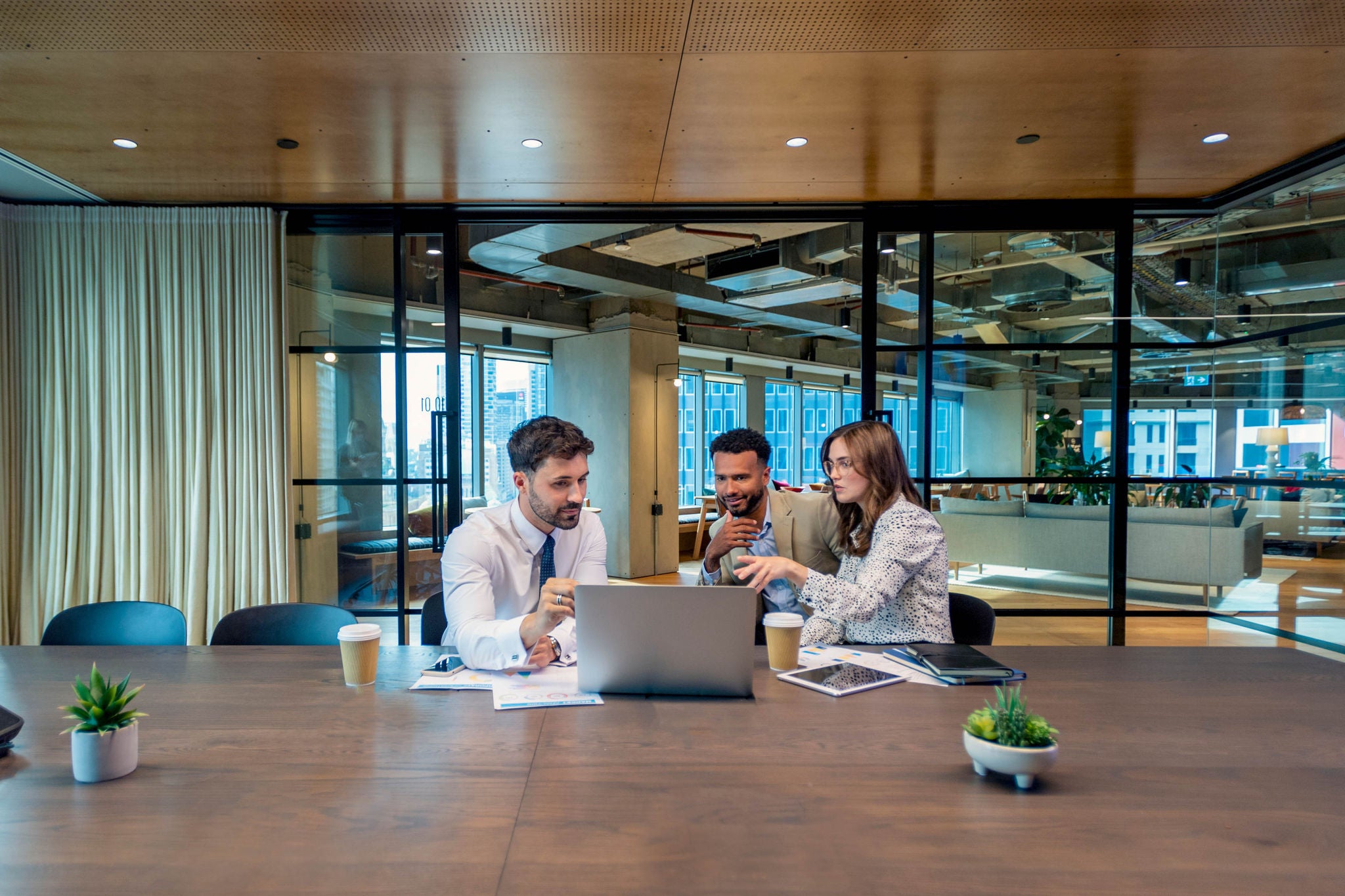 Business colleagues in a meeting, or Financial advisor or lawyer with couple explaining options. The agent is using a computer. All are well dressed. They sitting in an office meeting room. They are looking quite serious