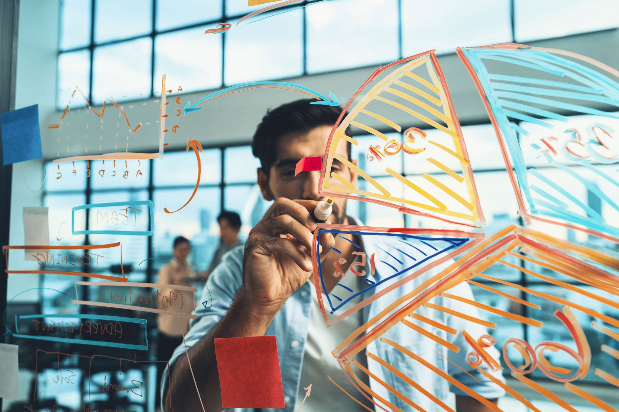 Portrait of young handsome businessman writing marketing idea by using colorful marker on glass wall with graph and mind map. Manager sharing idea or financial strategy. Business plan. Tracery.