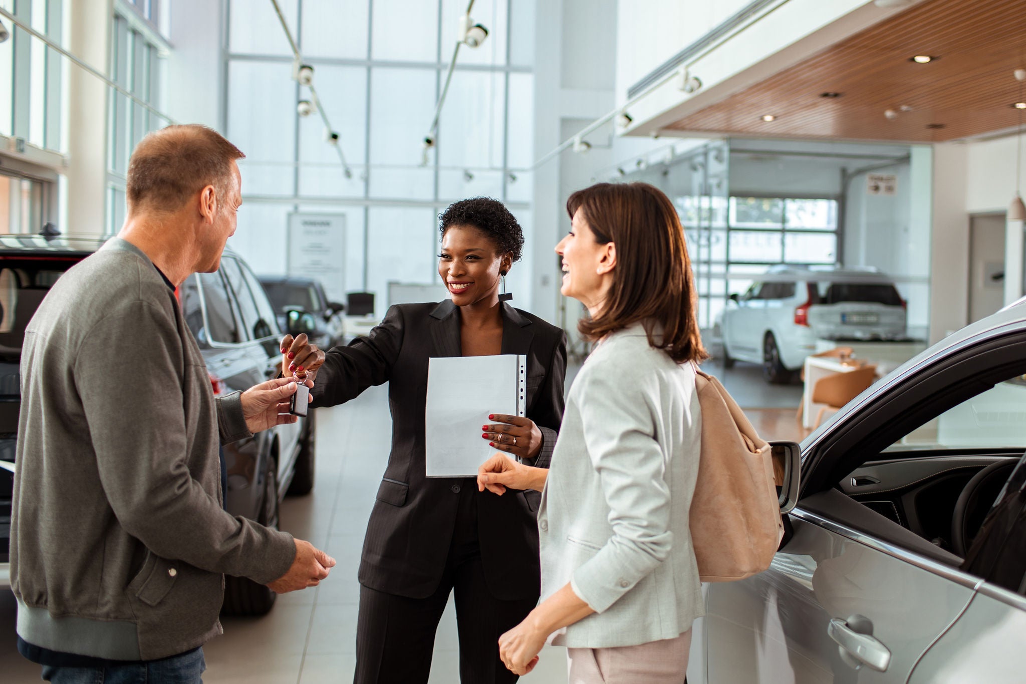 Couple signing paperwork to purchase a new car at dealership with saleswoman