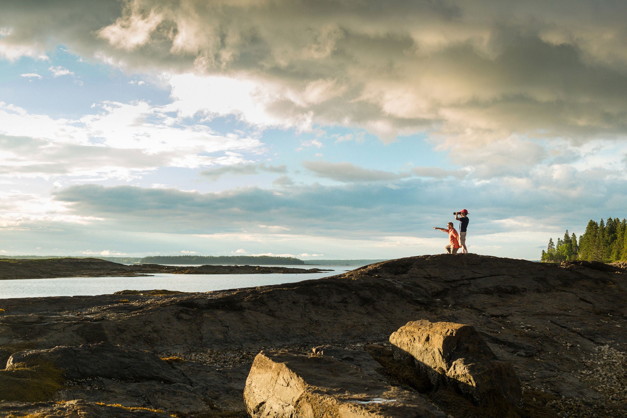 Distant view of senior man and son looking through binoculars at coast of Maine, USA