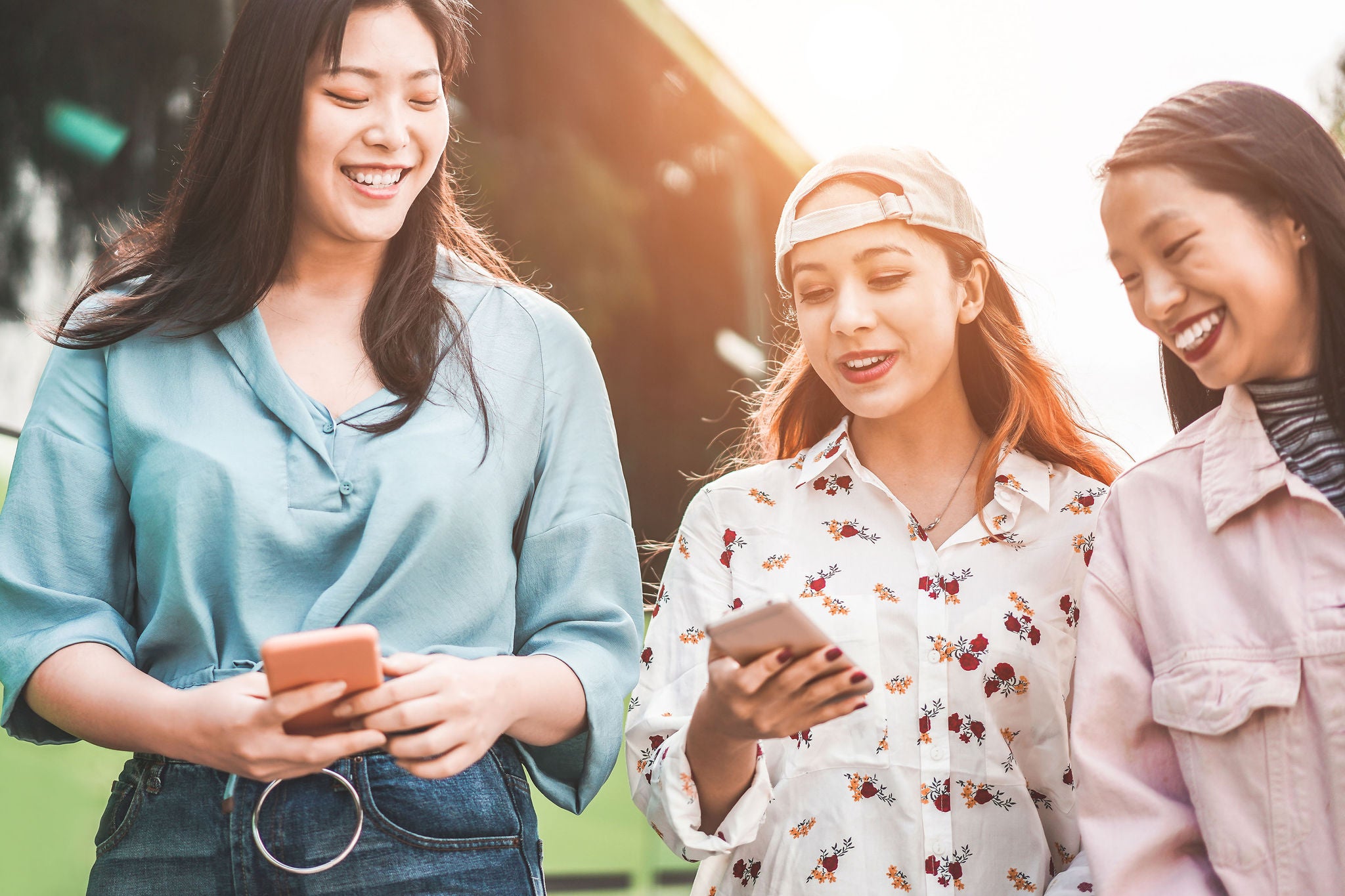 Three girls- smiling-and enjoying- together-while two of them-holding mobiles 