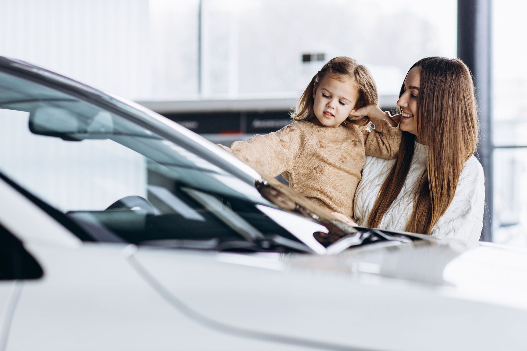 Mother with her little daughter choosing a car in a car showroom