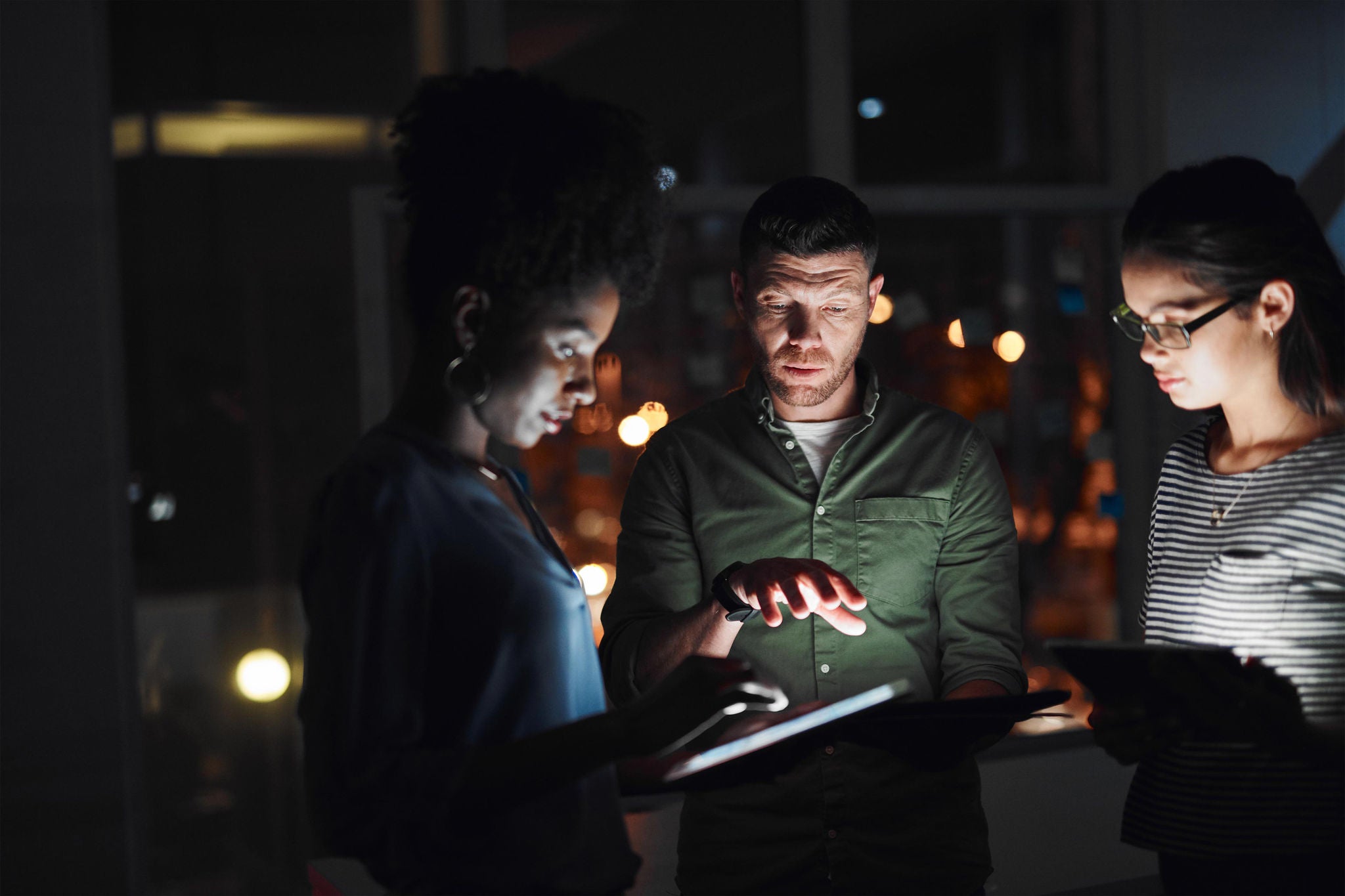 Aufnahme einer Gruppe von Geschäftsleuten, die nachts in einem Büro gemeinsam an einem digitalen Tablet arbeiten