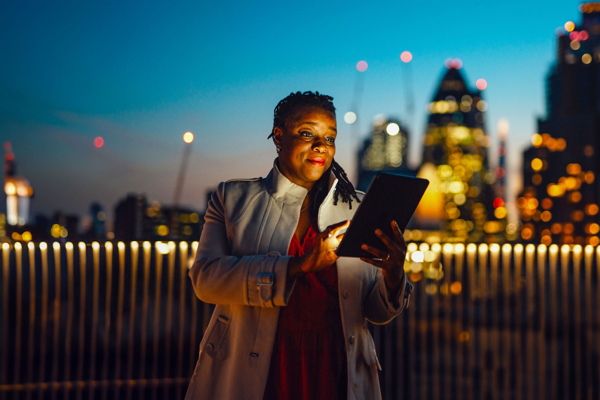 An adult African businesswoman using digital tablet at rooftop in business building against illuminated