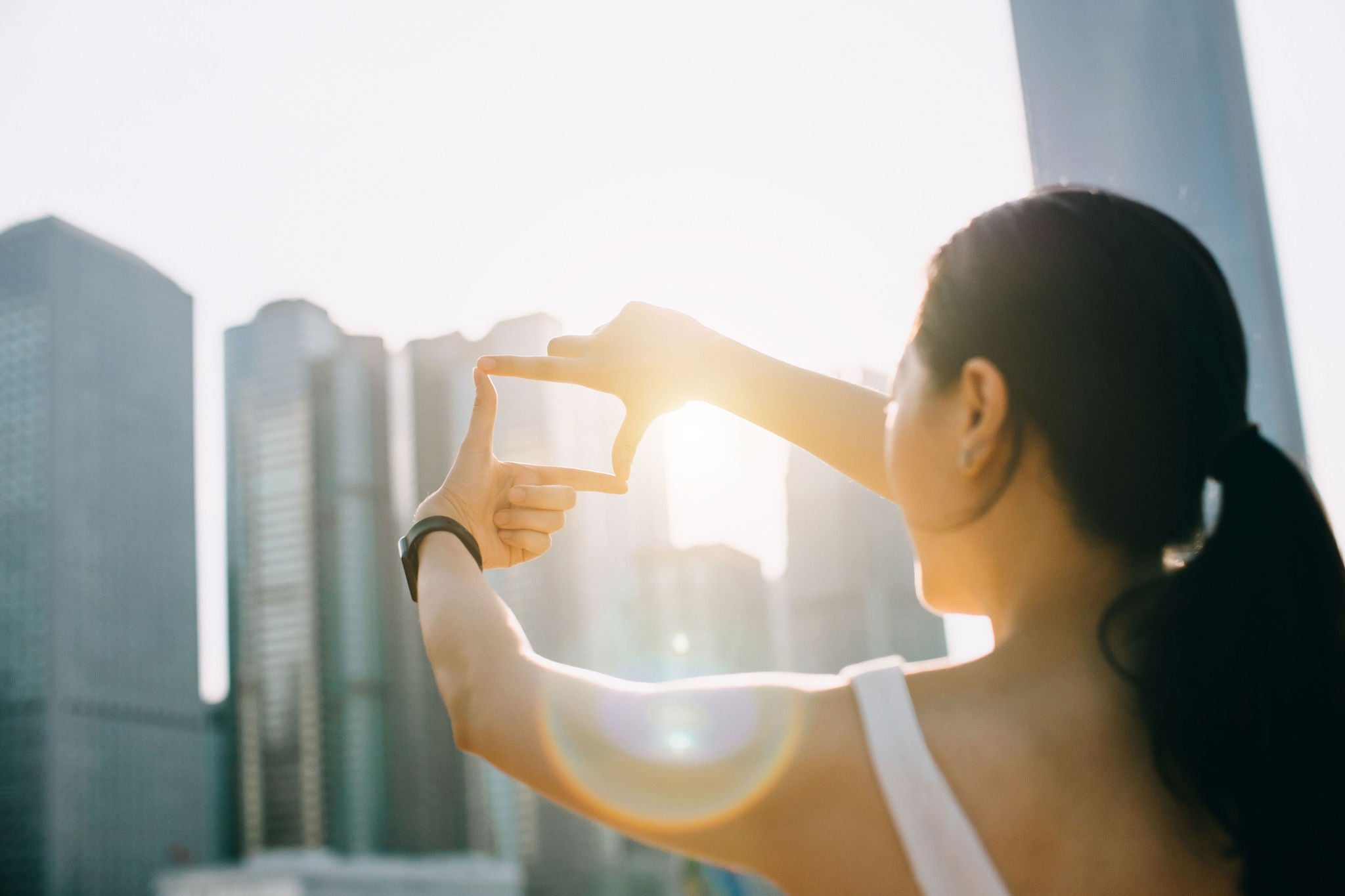 Young woman frames the Hong Kong city skyline into a finger frame under a sunny sky