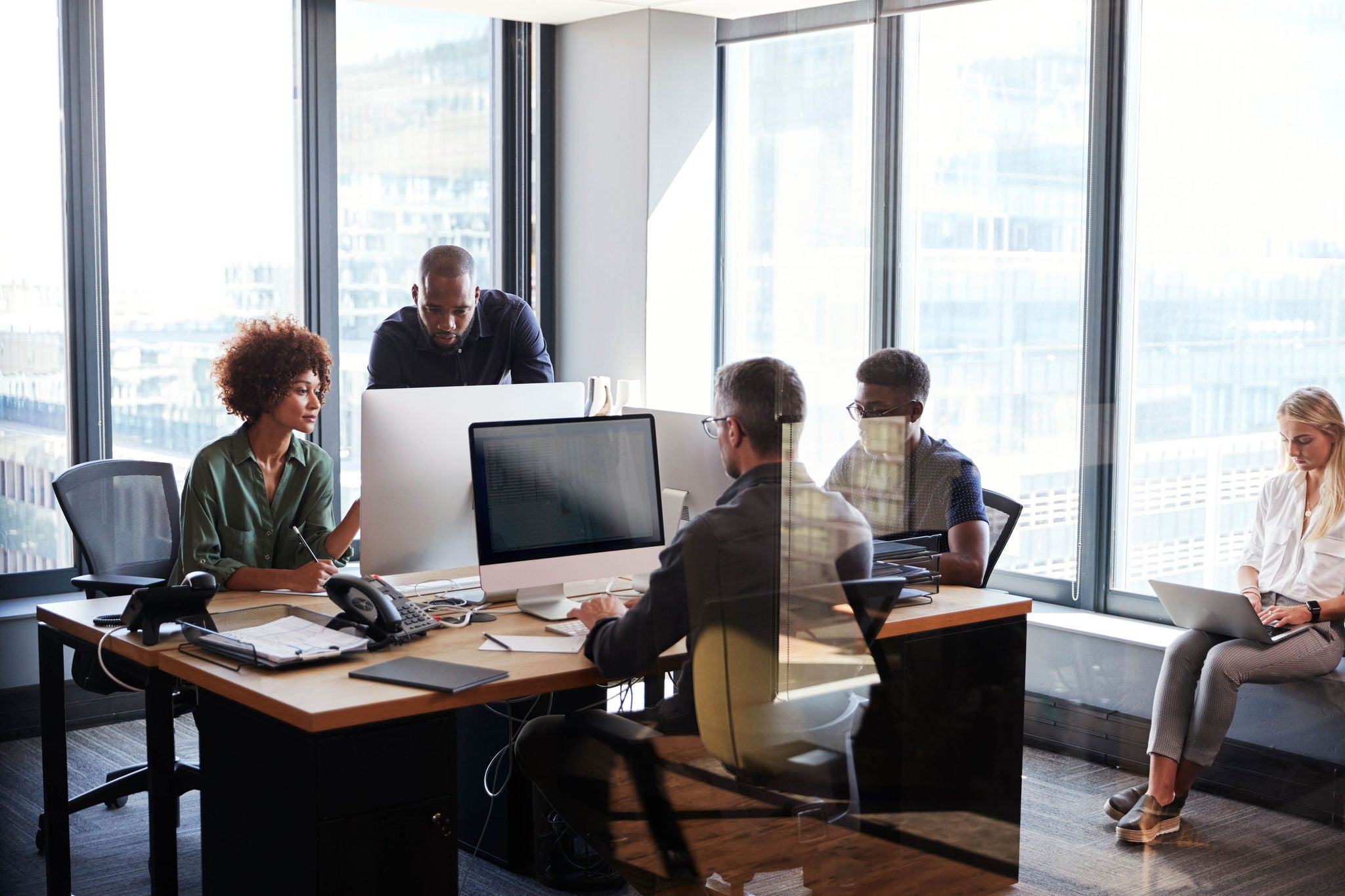 Young creative team working together at computers in a casual office, seen through glass wall