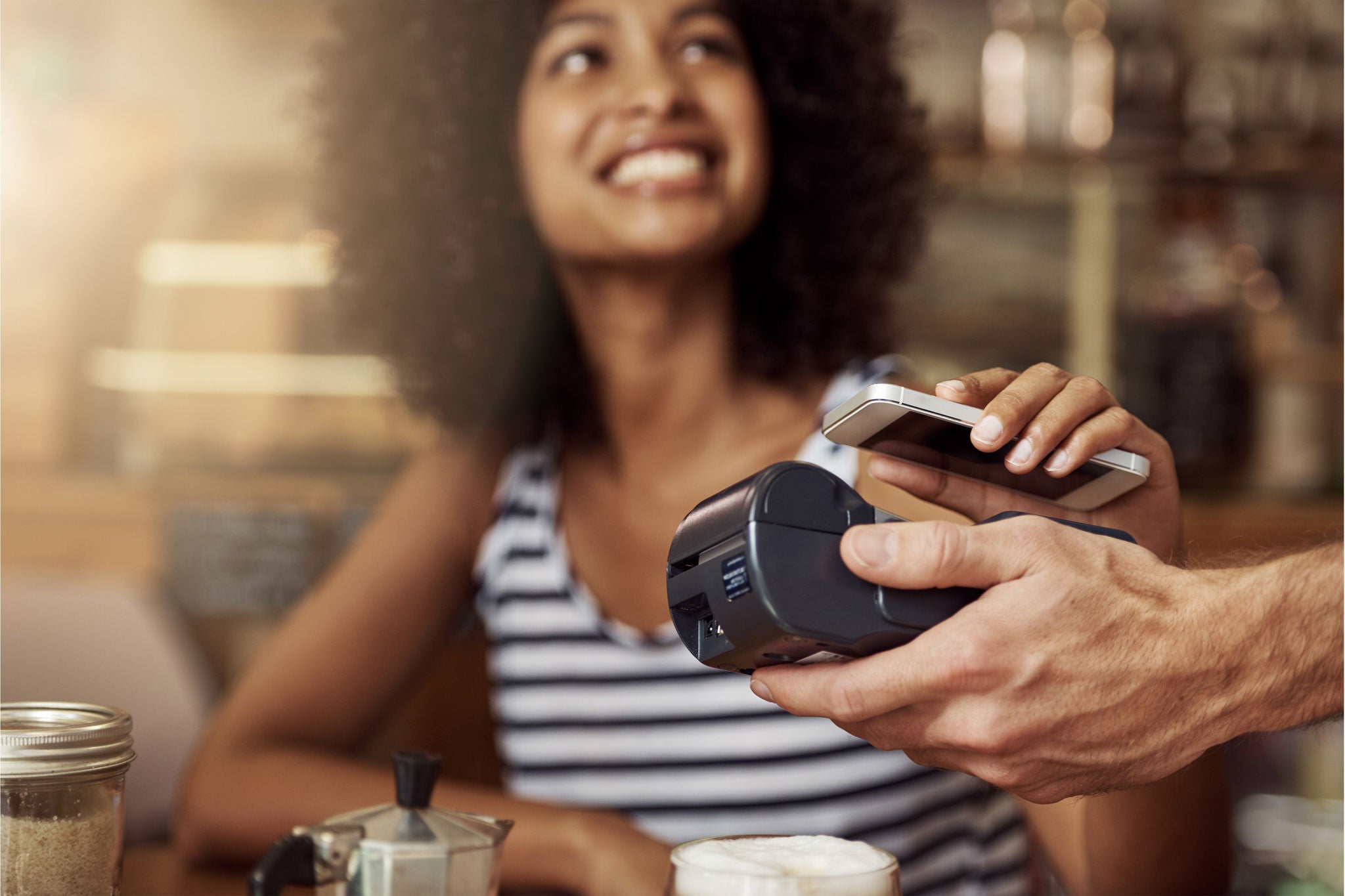 Shot of a beautiful woman using her smart phone and an electronic reader to pay her bill in a coffee shop