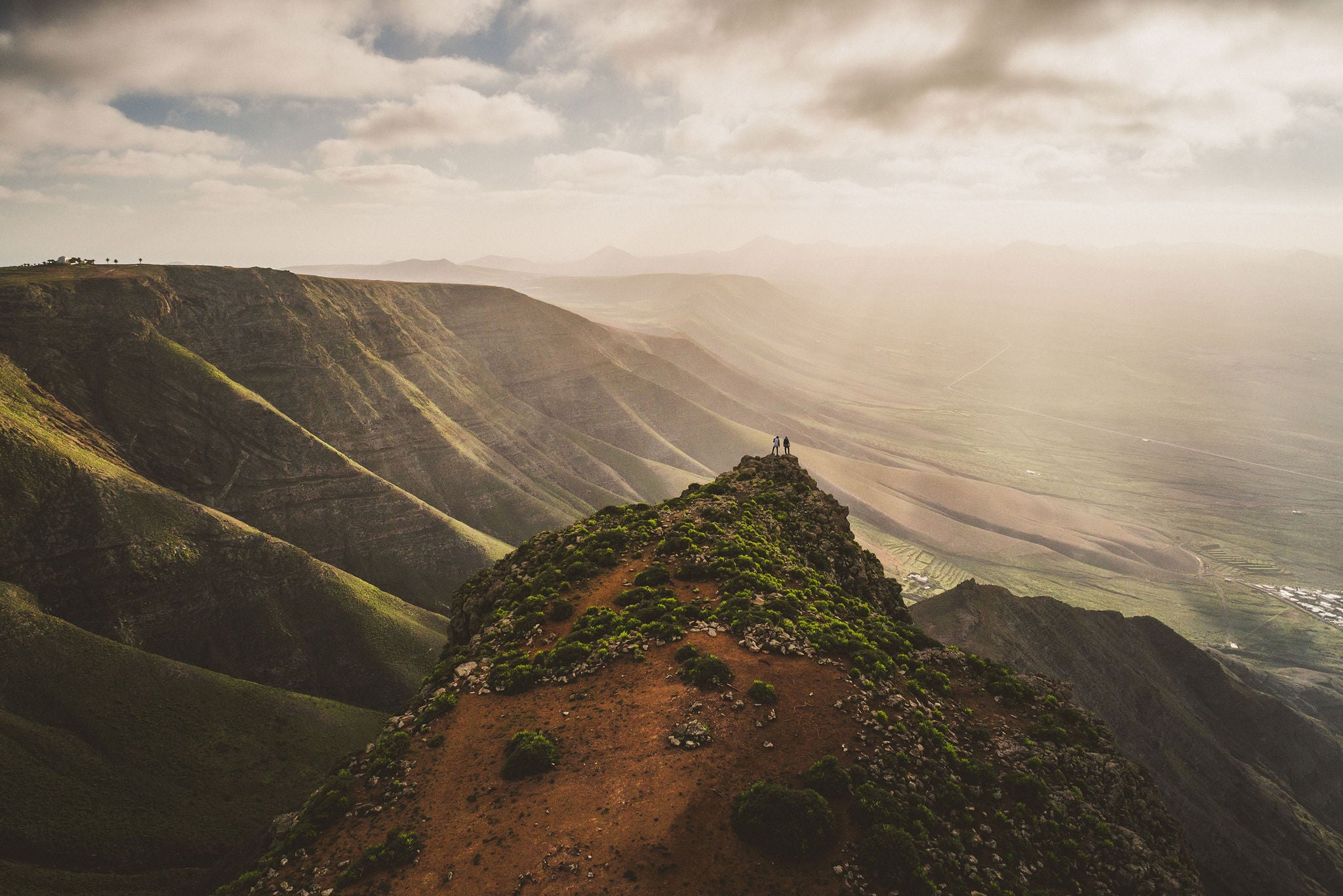 Two people standing at the edge of the hill top in nature